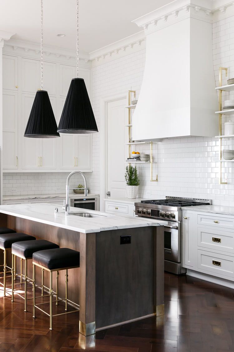 Modern white kitchen with dark wood island, black pendant lights, and stools on a hardwood floor.