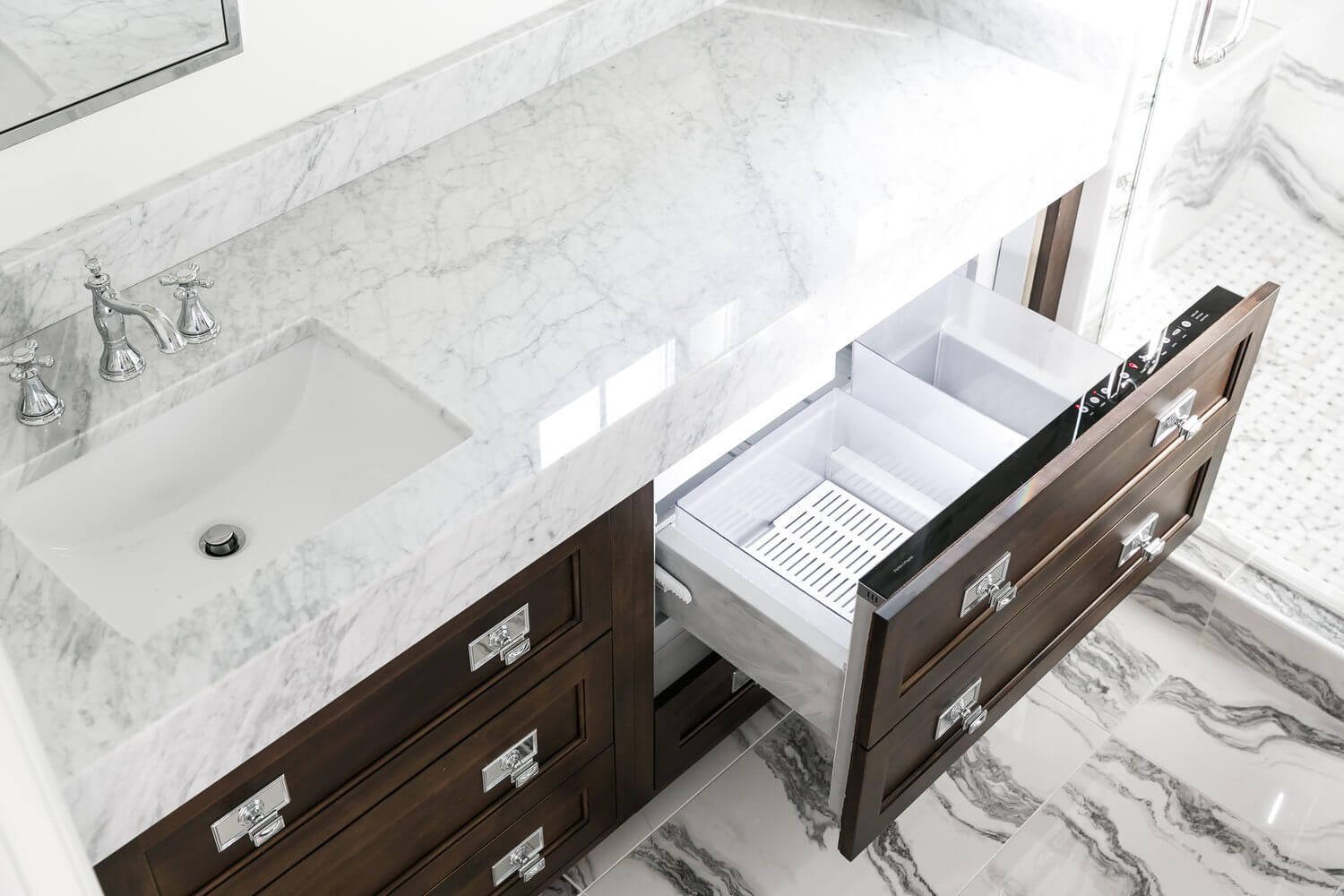 Marble bathroom vanity with sink and open drawers, showing interior storage organizers.