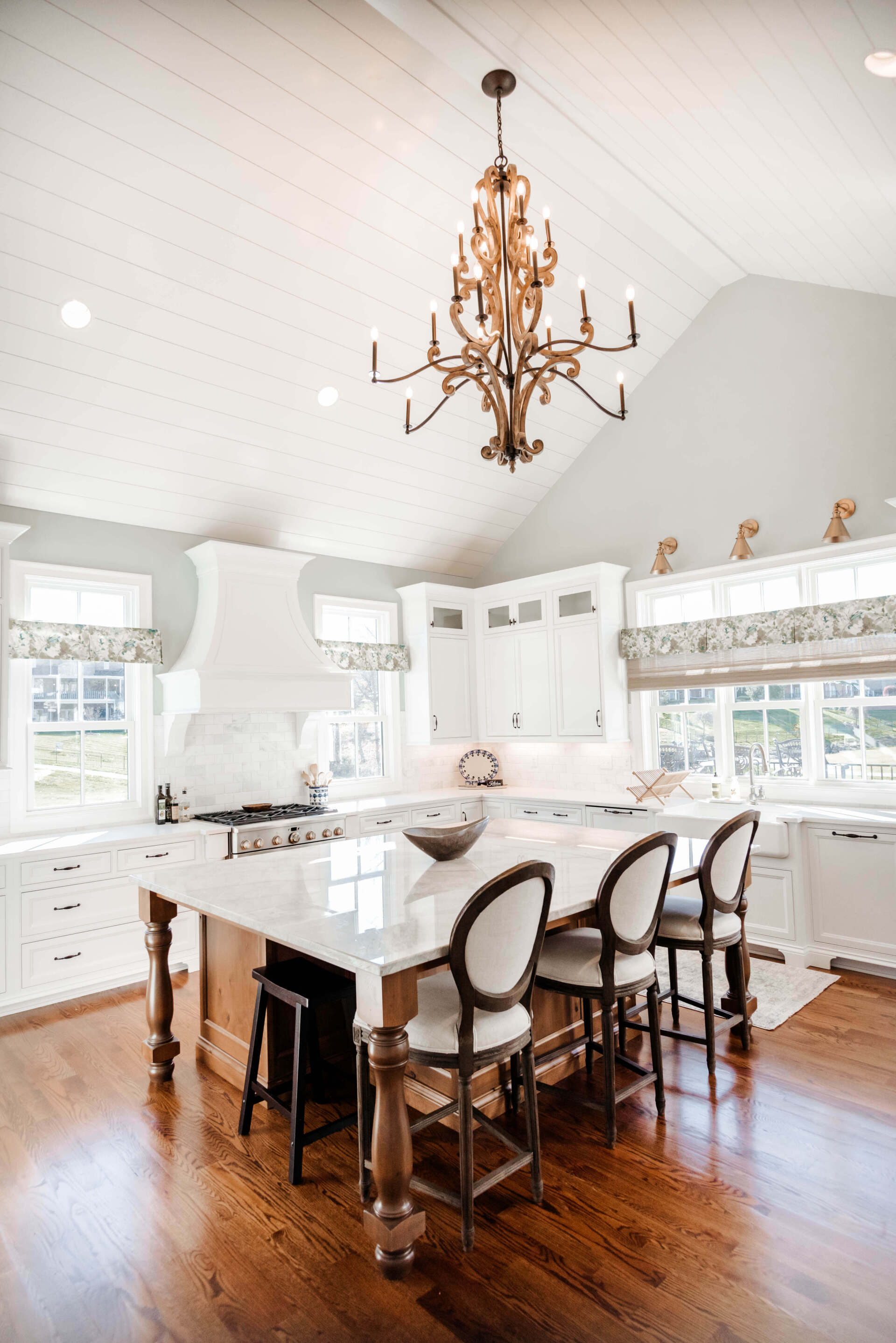 Bright kitchen with white cabinetry, large island, and ornate chandelier over polished wood floor