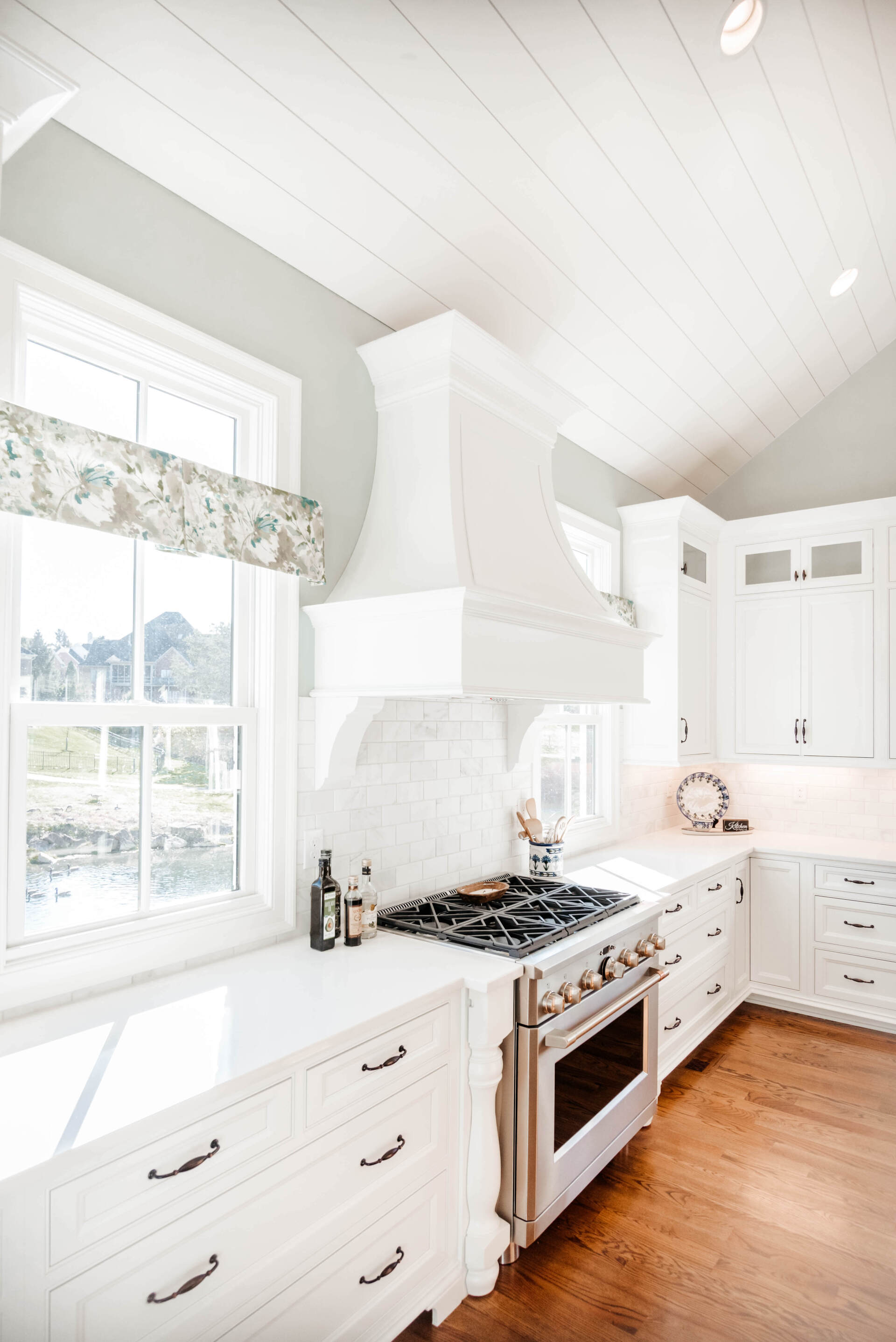 Bright white kitchen with farmhouse sink, gas range, and wood floors under a vaulted ceiling.