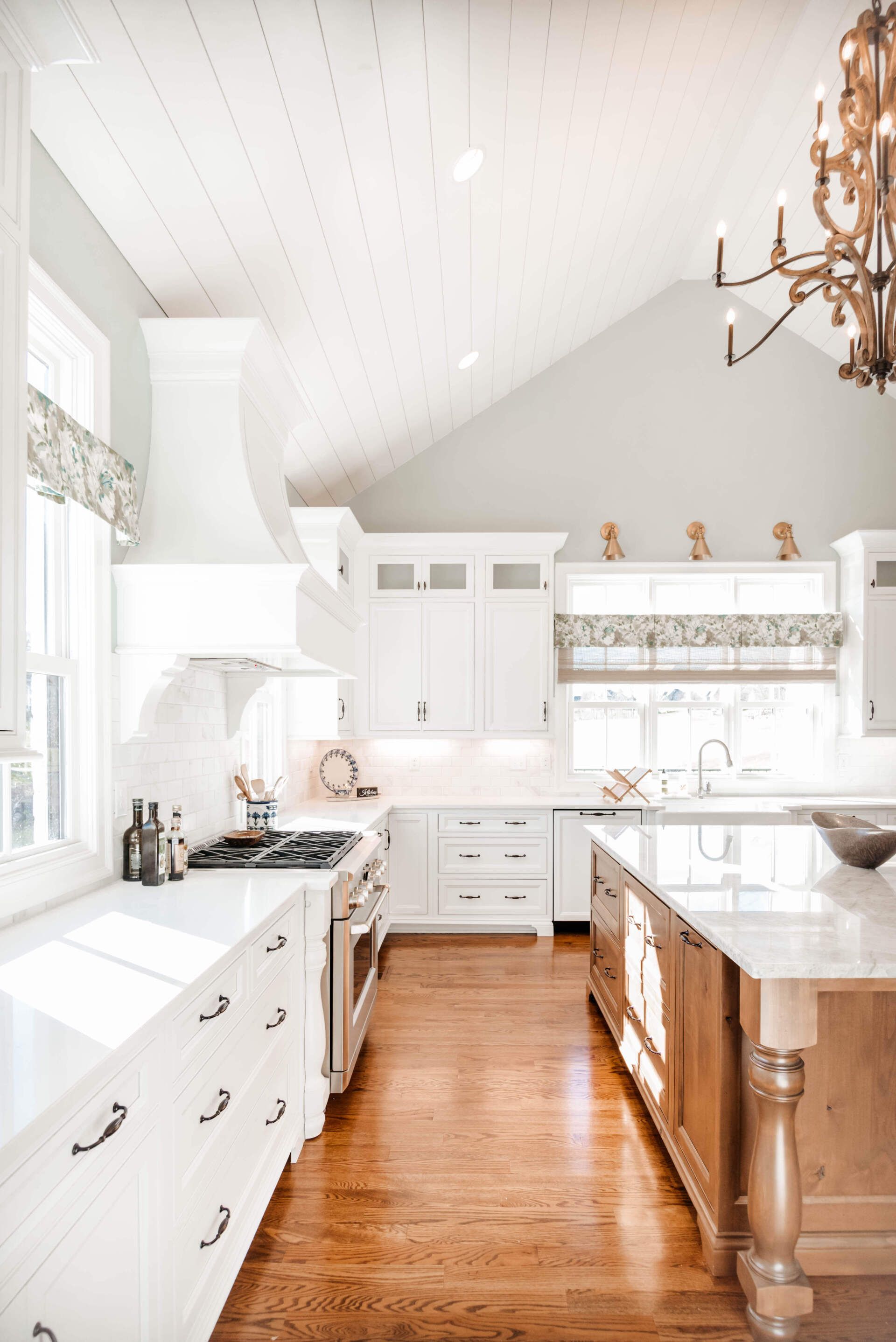 Bright white kitchen with wood floors, island, and large windows, lit by natural light