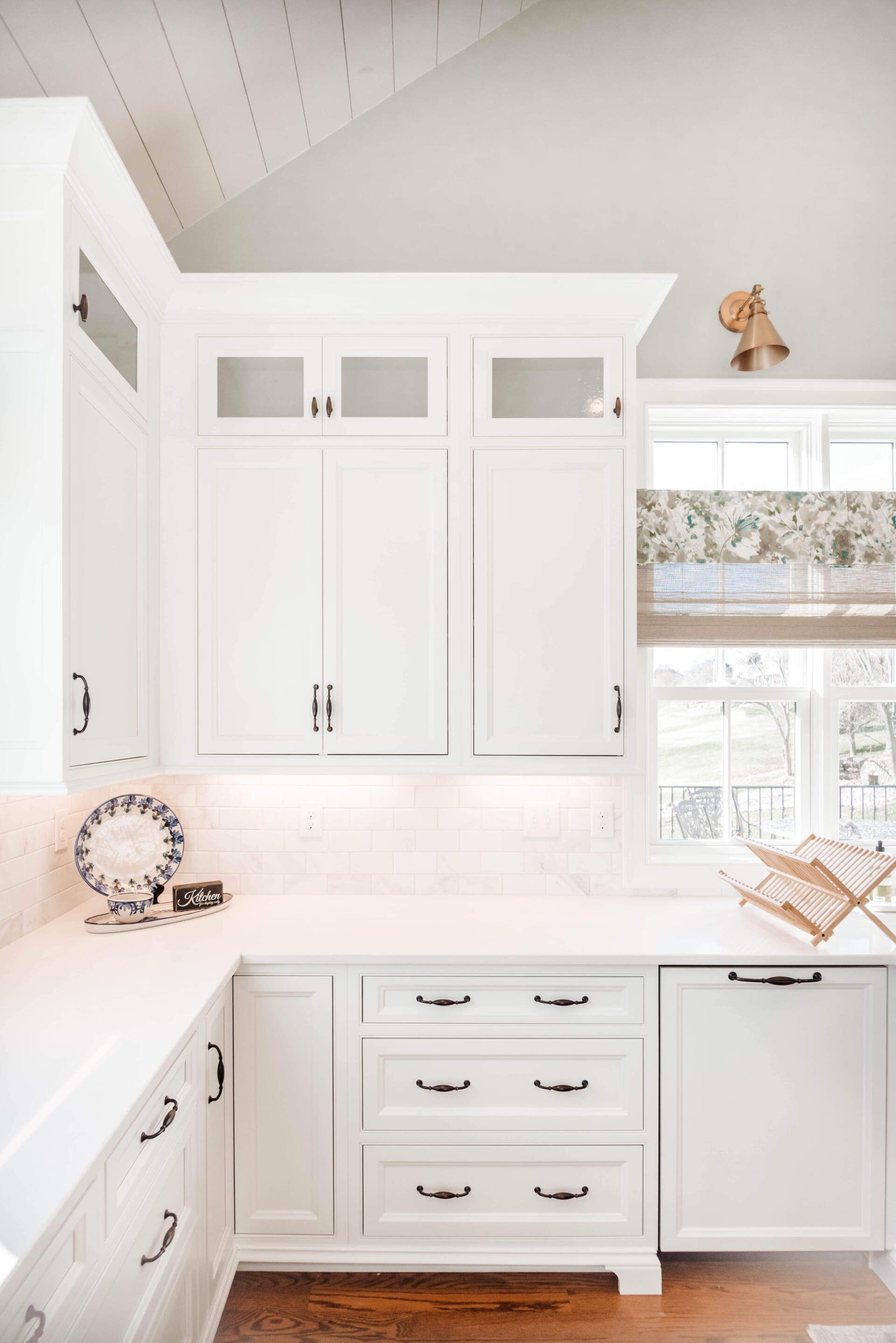 Bright white kitchen with built-in cabinets, drawers, window, and small decorative accents