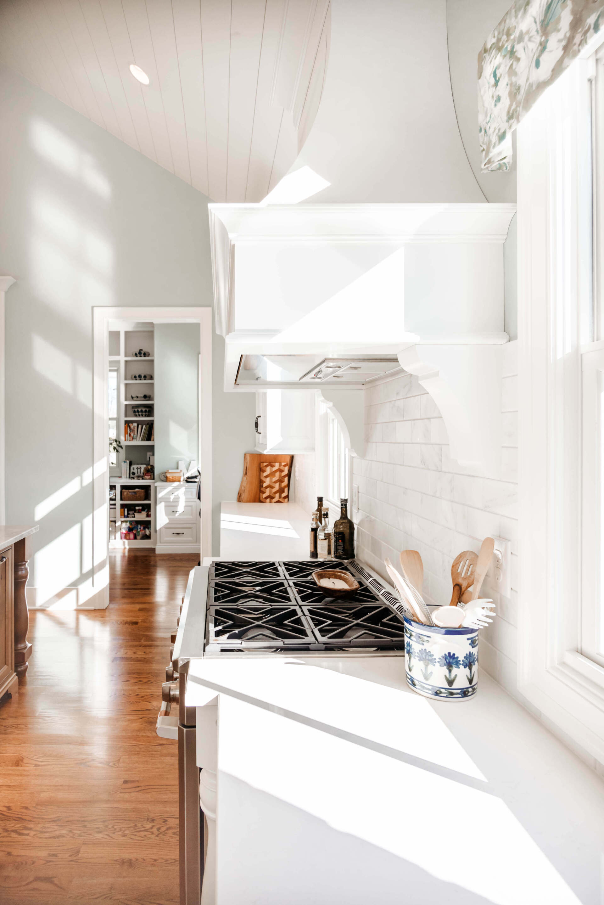 Bright white kitchen with a black patterned runner and sunlit wooden floor corridor.