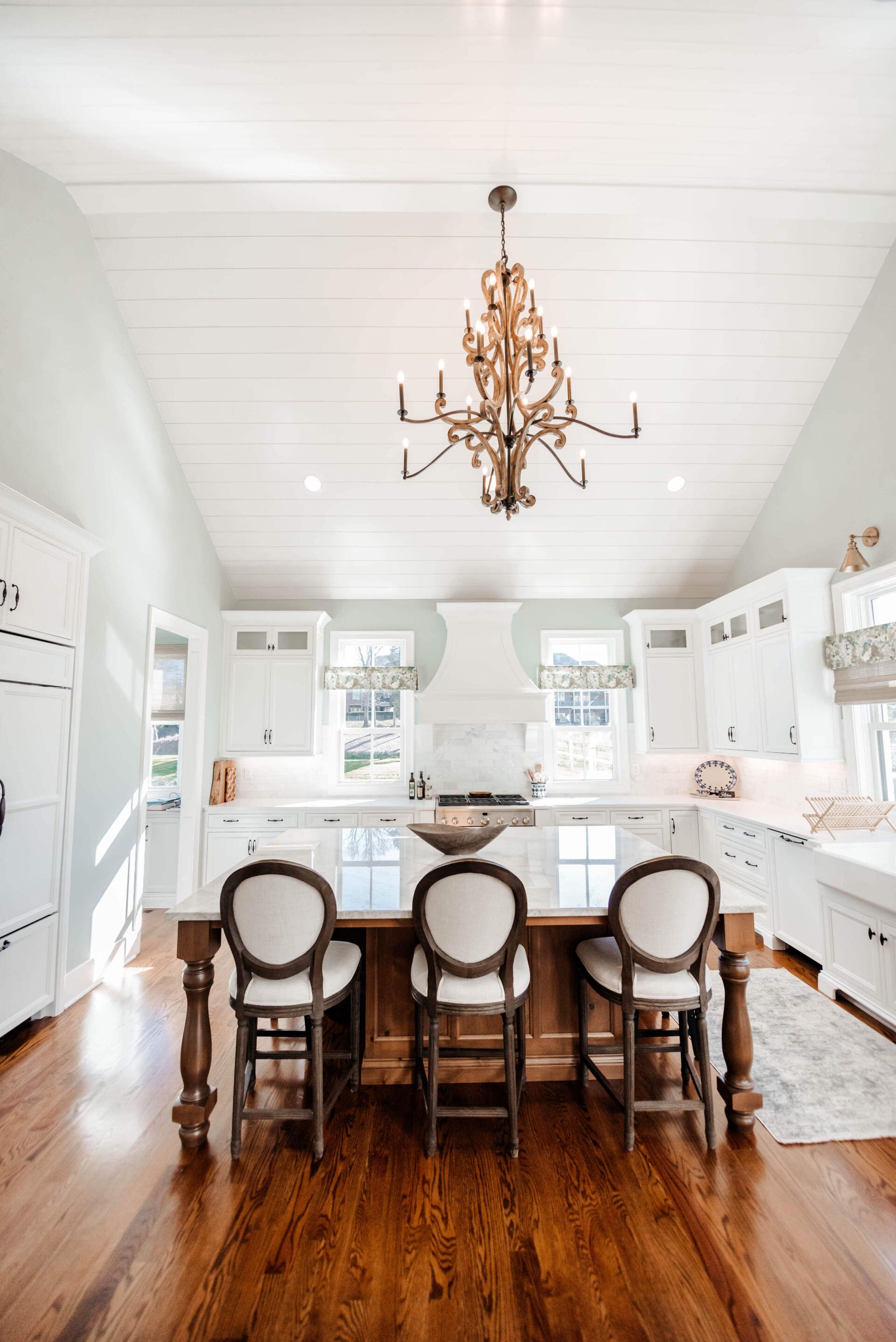 Bright white kitchen with island seating, brass chandelier, and warm wood floors