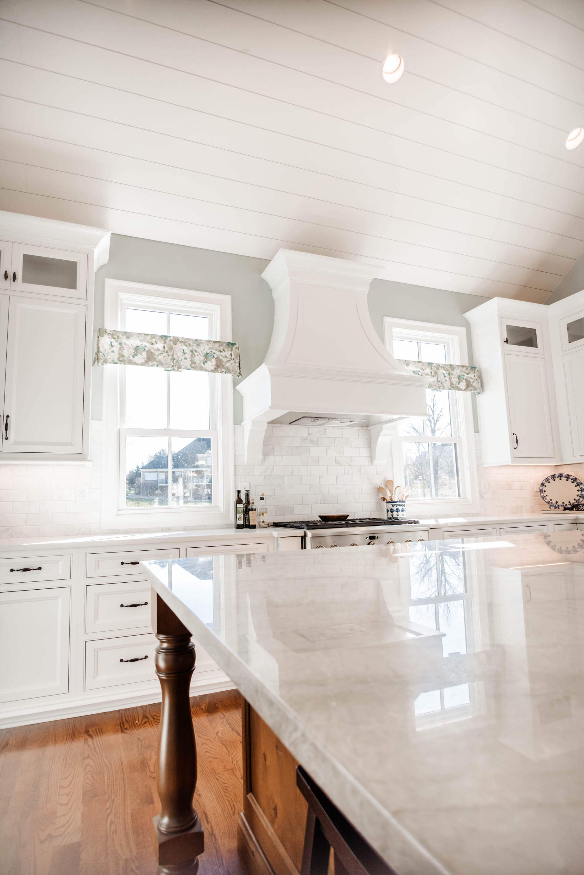 Bright white kitchen with marble island, large windows, and wooden floorboards