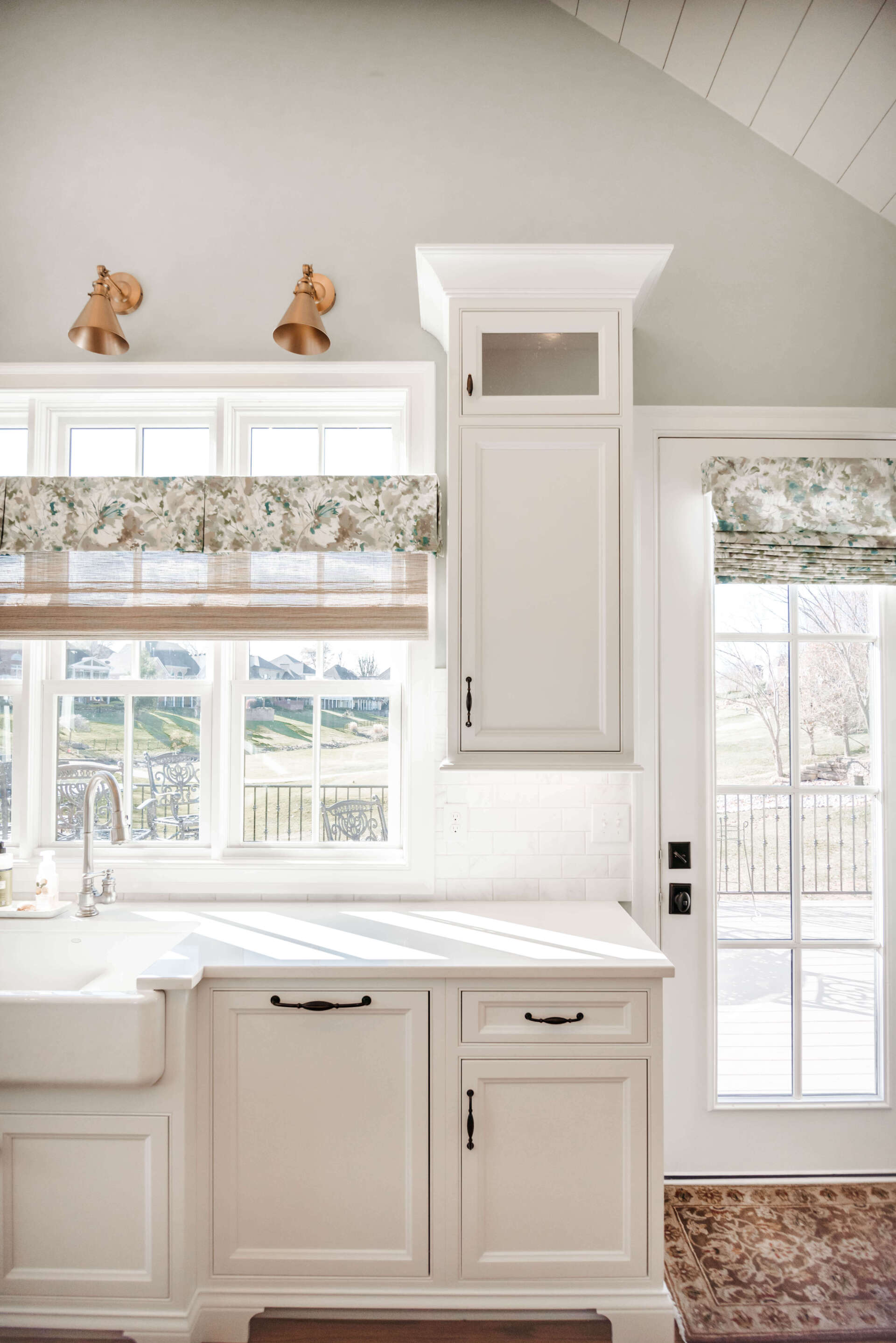 Bright white kitchen with cabinets, windows, patterned shades, and two small animal figurines on top.