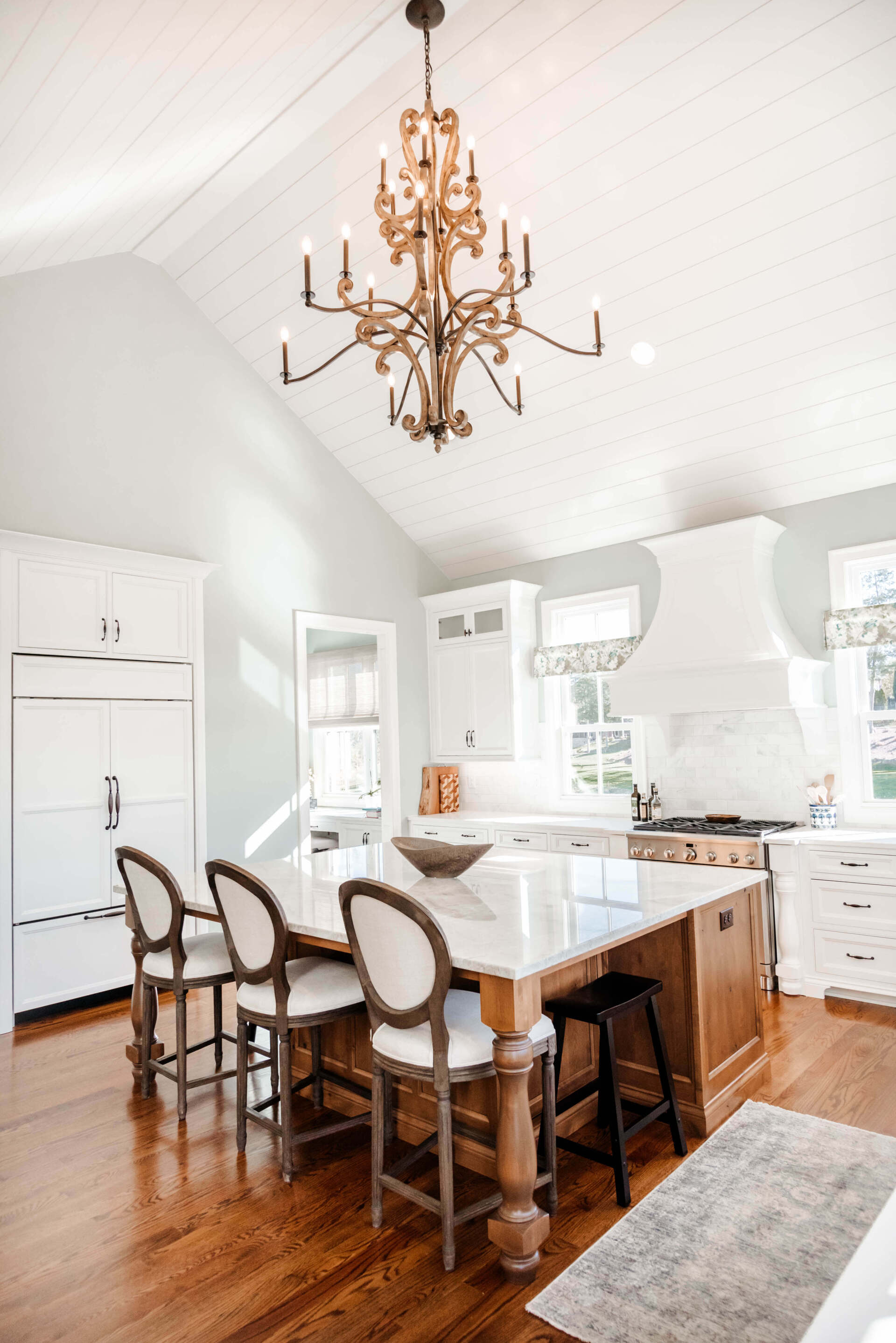 Bright white kitchen with island, bar stools, chandelier, and hardwood floors
