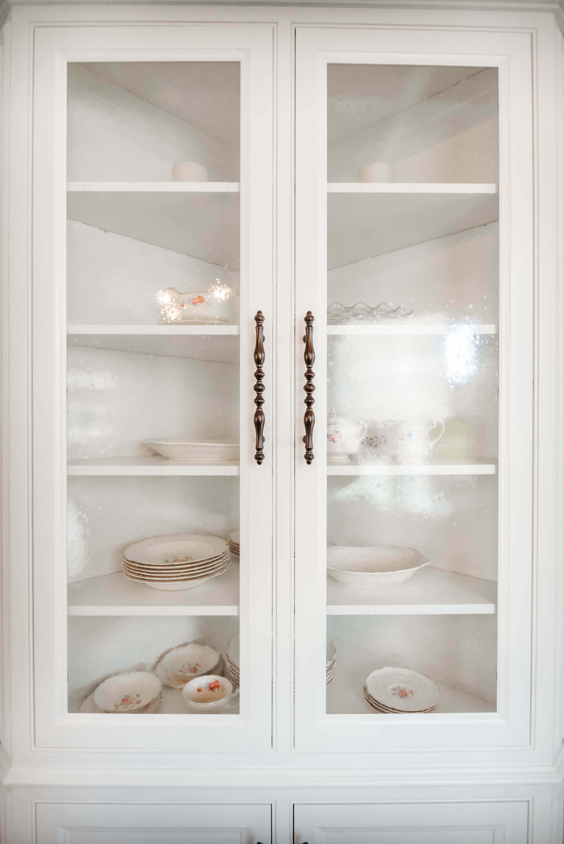White glass-front cabinet with shelves displaying plates and bowls