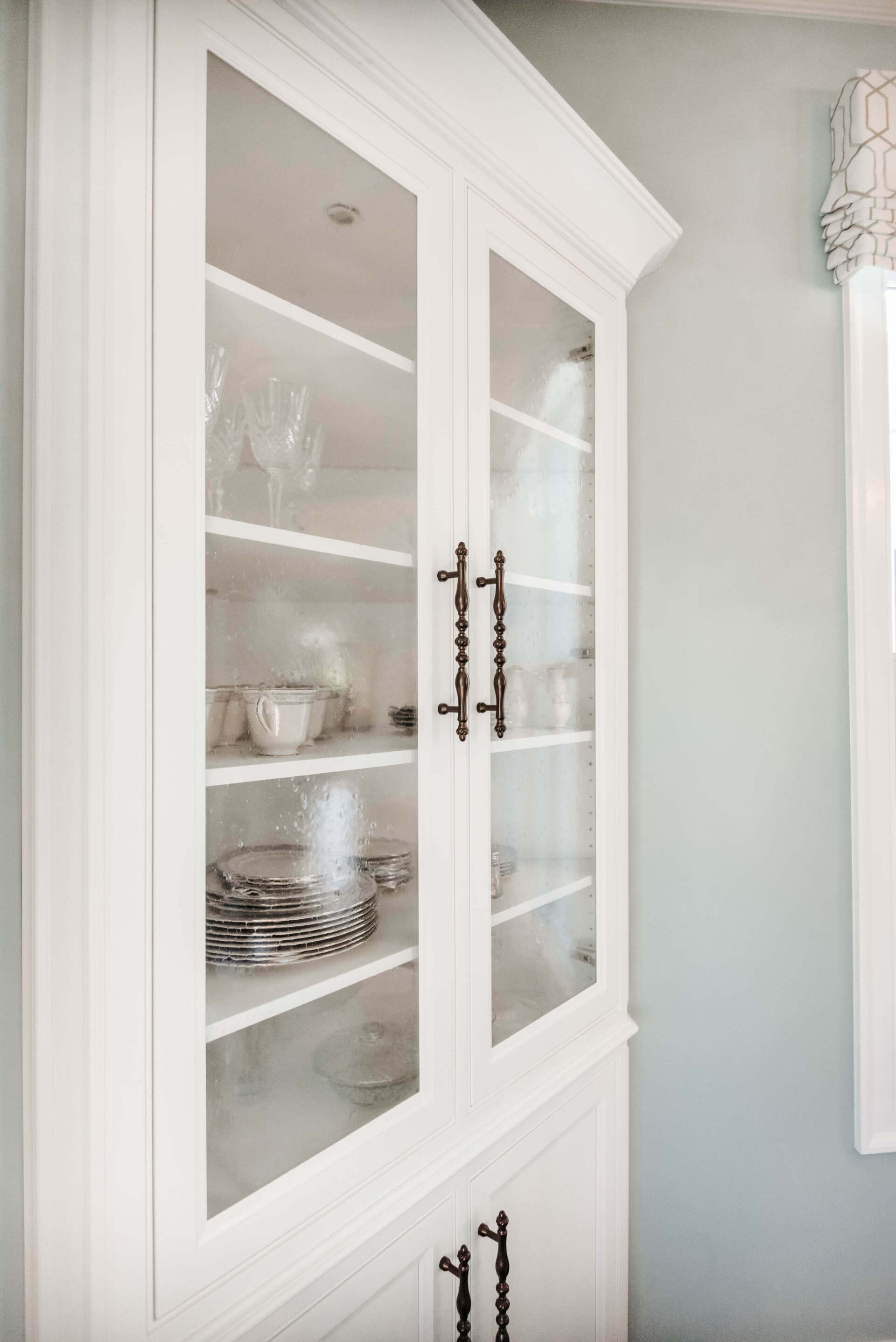 White glass-front cabinet with shelves holding dishes in a bright room