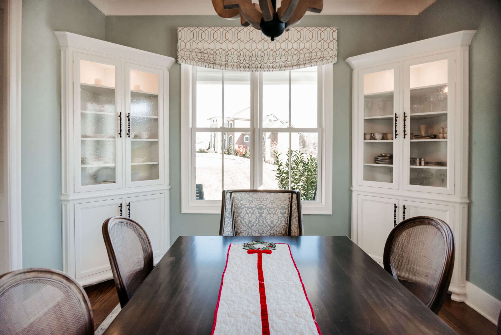 Bright dining room with a dark table, upholstered chairs, white cabinets, and a large window.