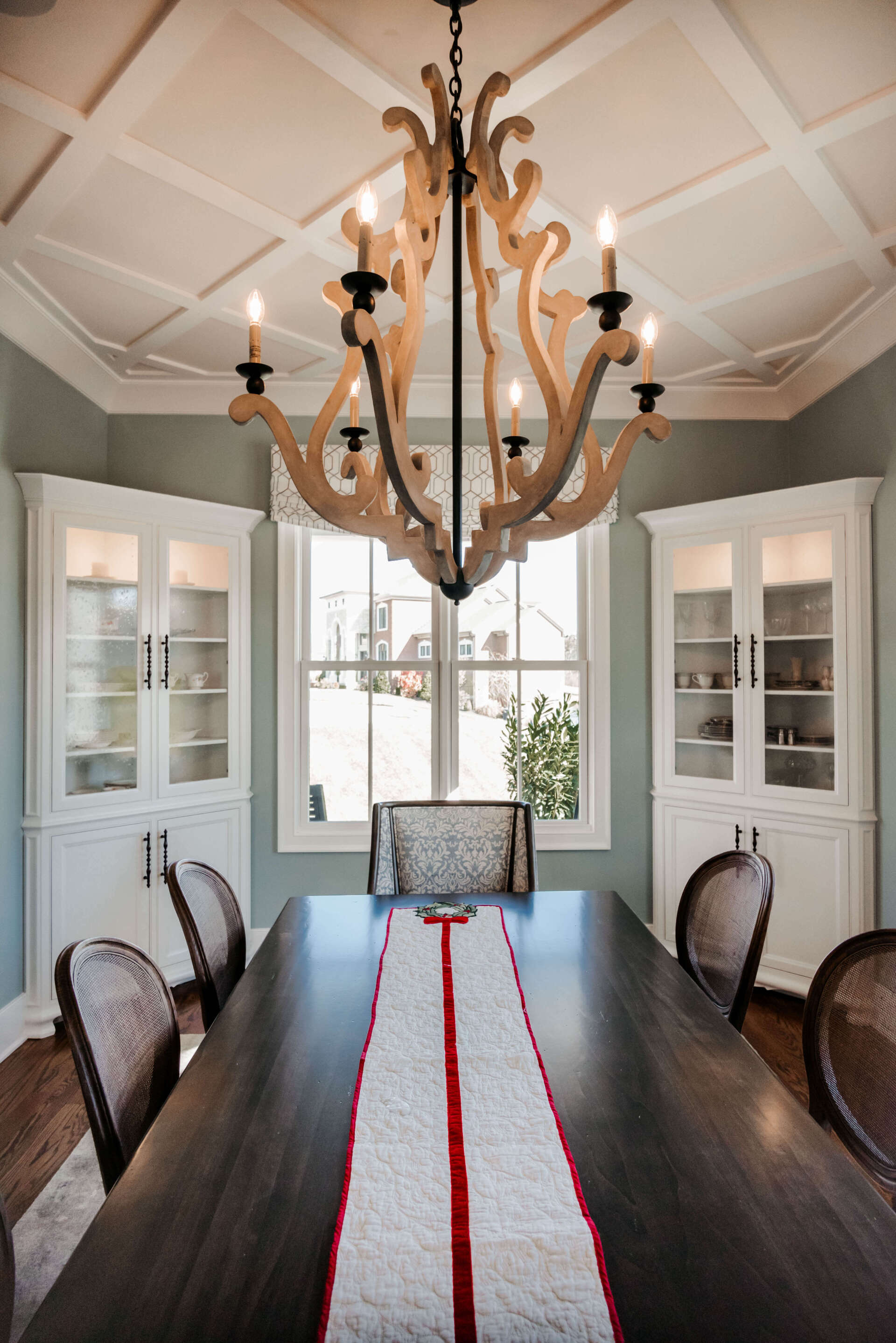 Elegant dining room with dark wood table, chandelier, bay windows, and white built-in cabinets.