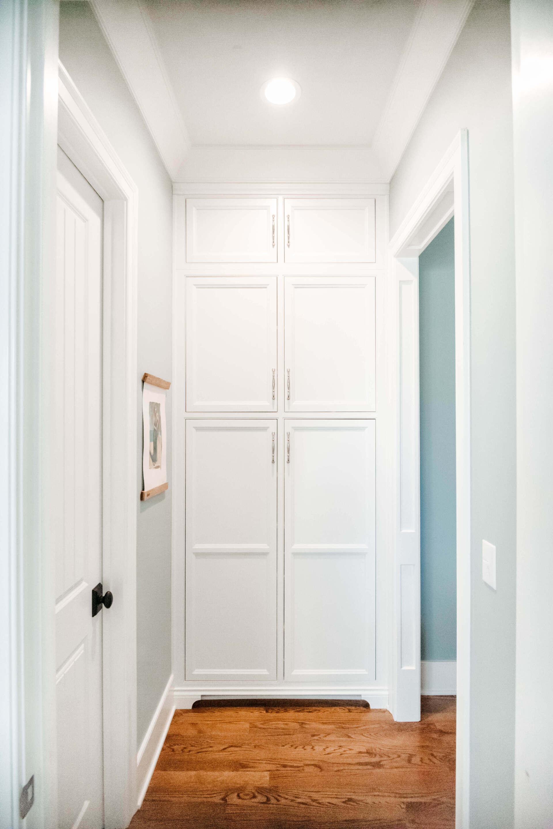 Bright white hallway with a wood floor and built-in cabinets at the end, flanked by doorways.