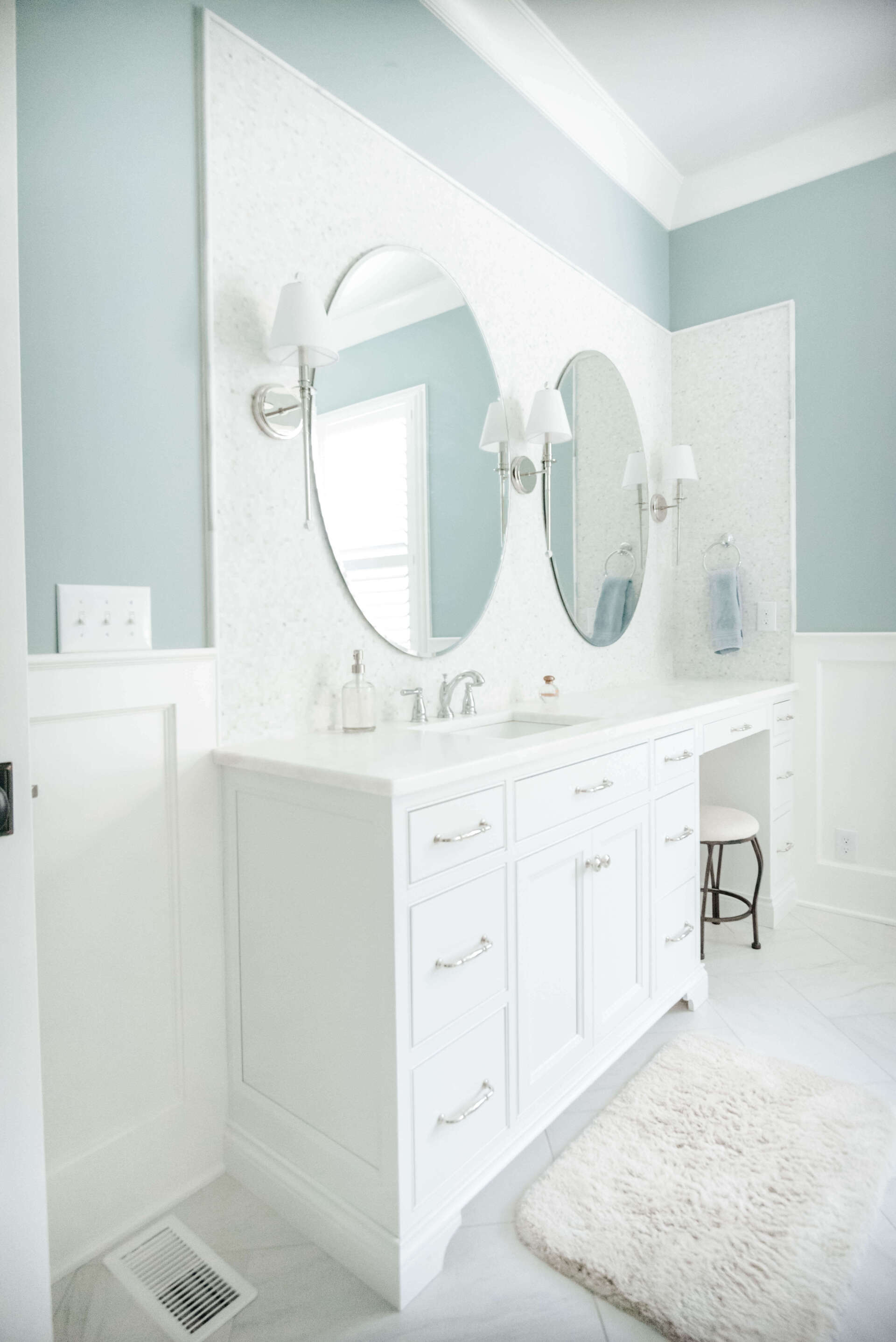 Bright white bathroom vanity with round mirrors, gray walls, and a fluffy rug