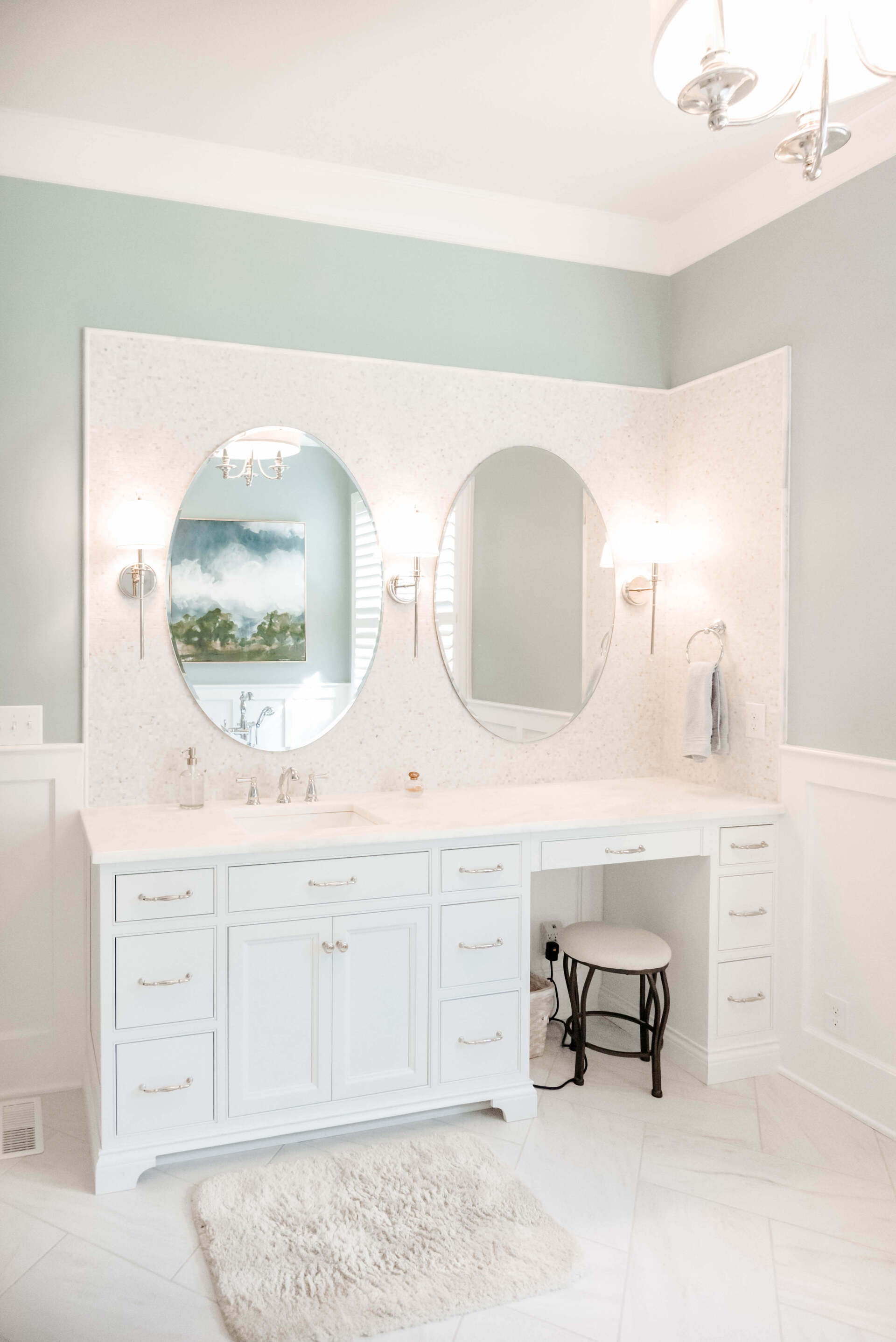 Elegant white bathroom vanity with twin oval mirrors, mint walls, and a fluffy rug