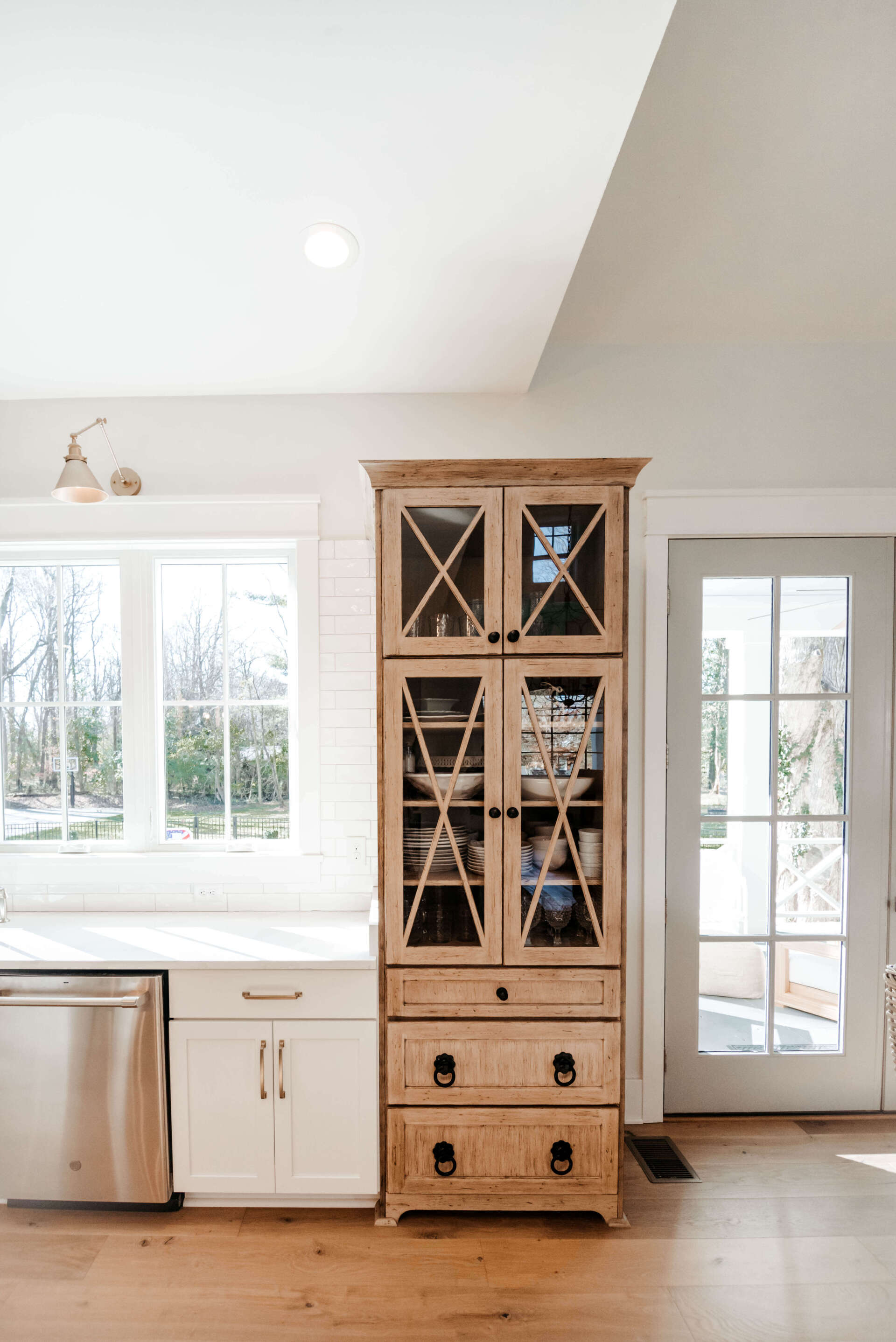 Bright kitchen with white cabinets, large windows, and a tall wooden hutch against the wall.