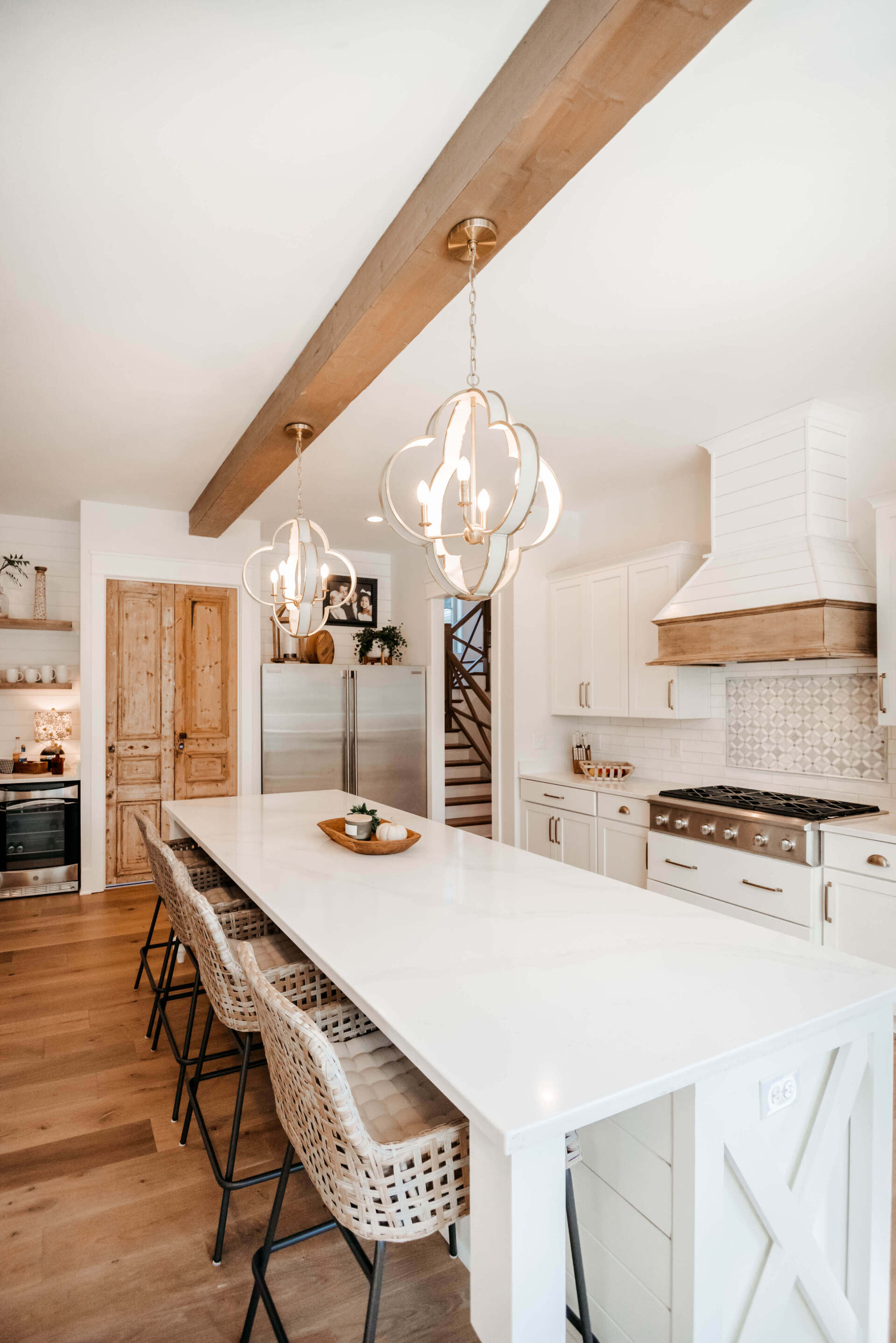 Bright farmhouse kitchen with long white island, wood beam ceiling, wicker stools, and pendant lights