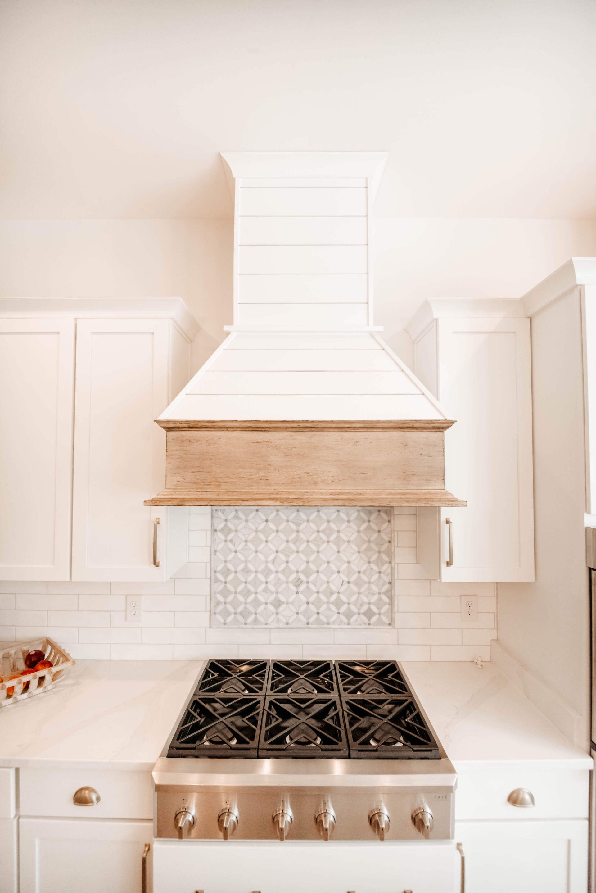 White kitchen with a stainless range, custom hood, and light cabinetry on both sides.
