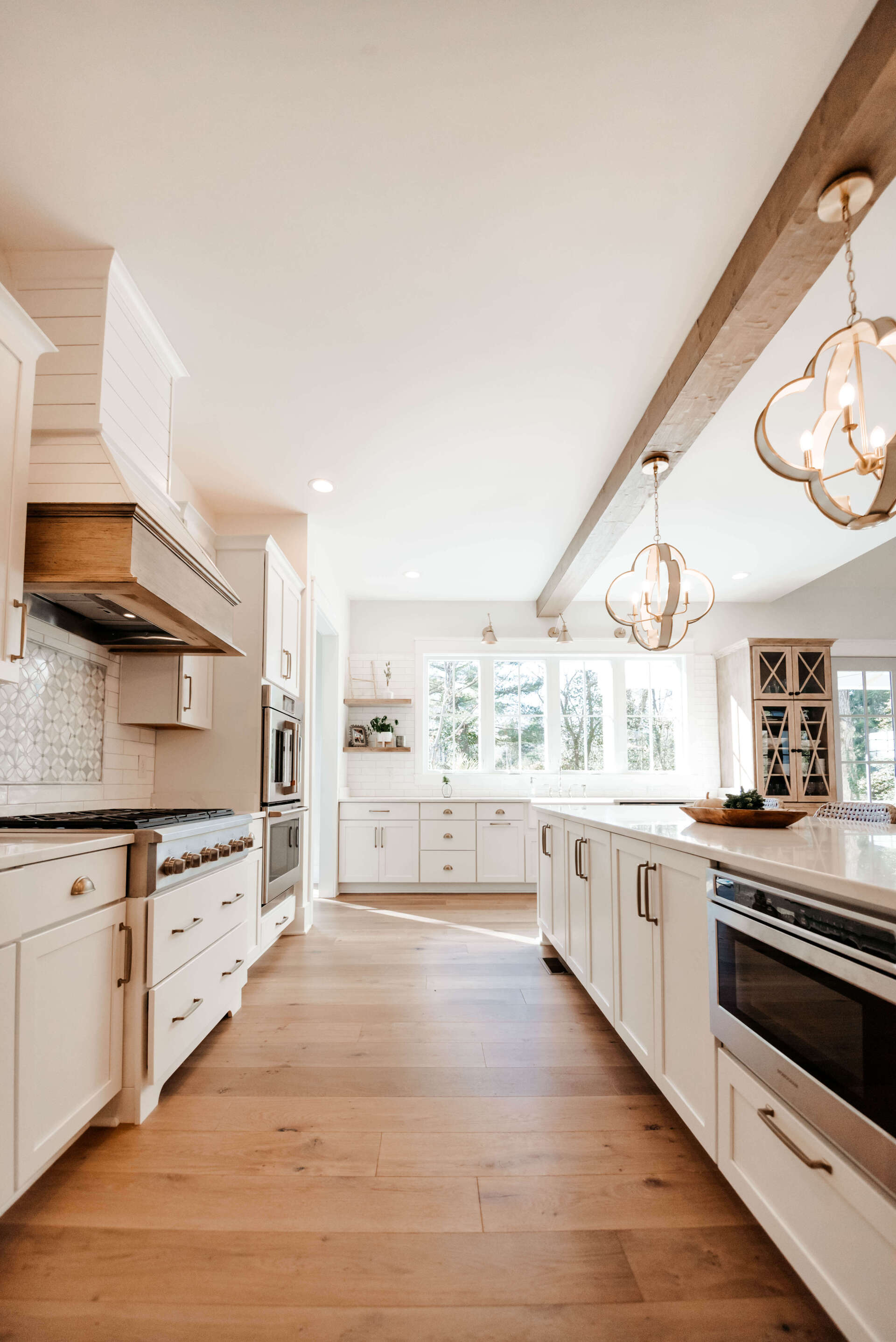 Bright white kitchen with wood floors, island, stainless oven, and pendant lights by a window