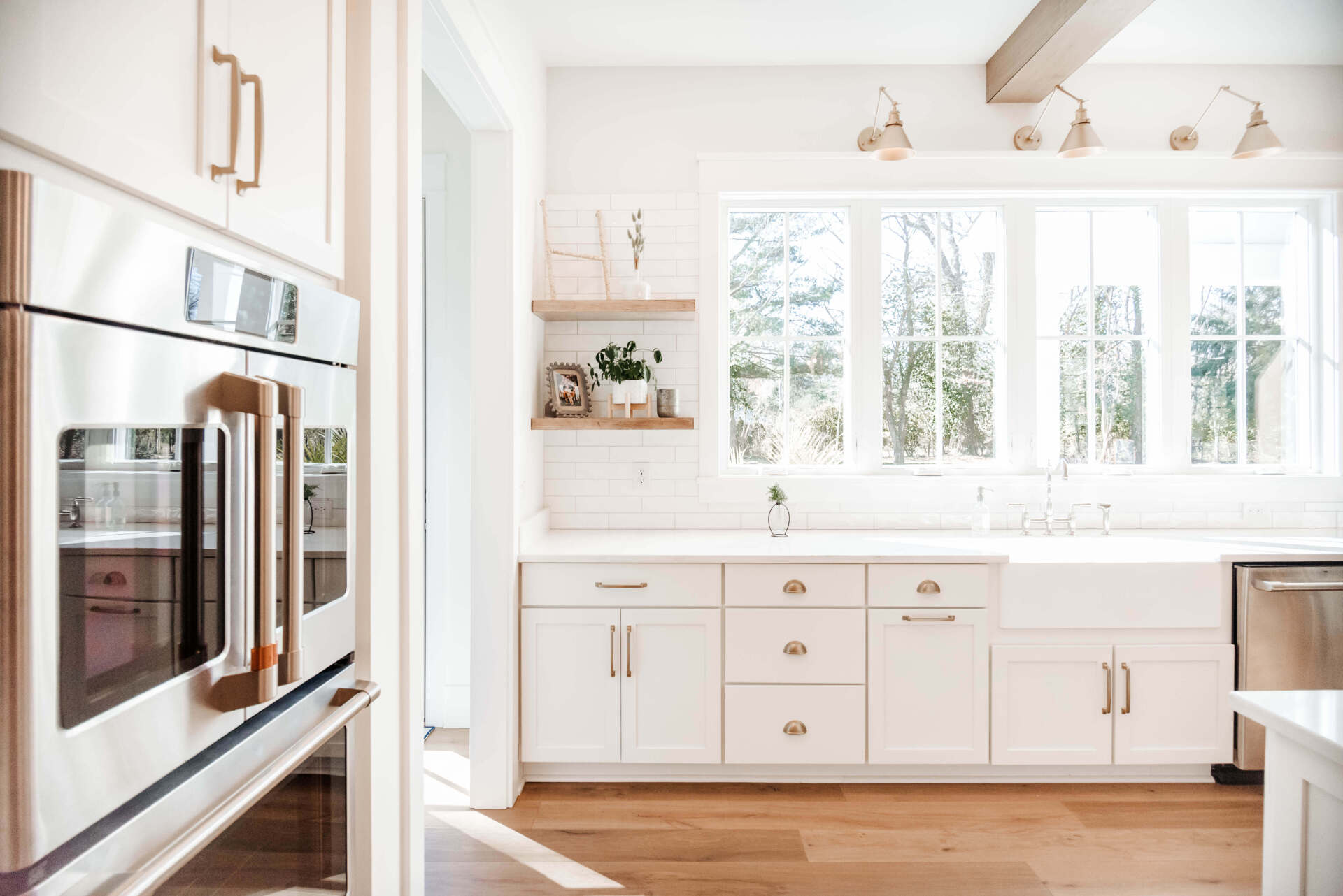 Bright white modern kitchen with built-in oven, farmhouse sink, and sunlit window above cabinets