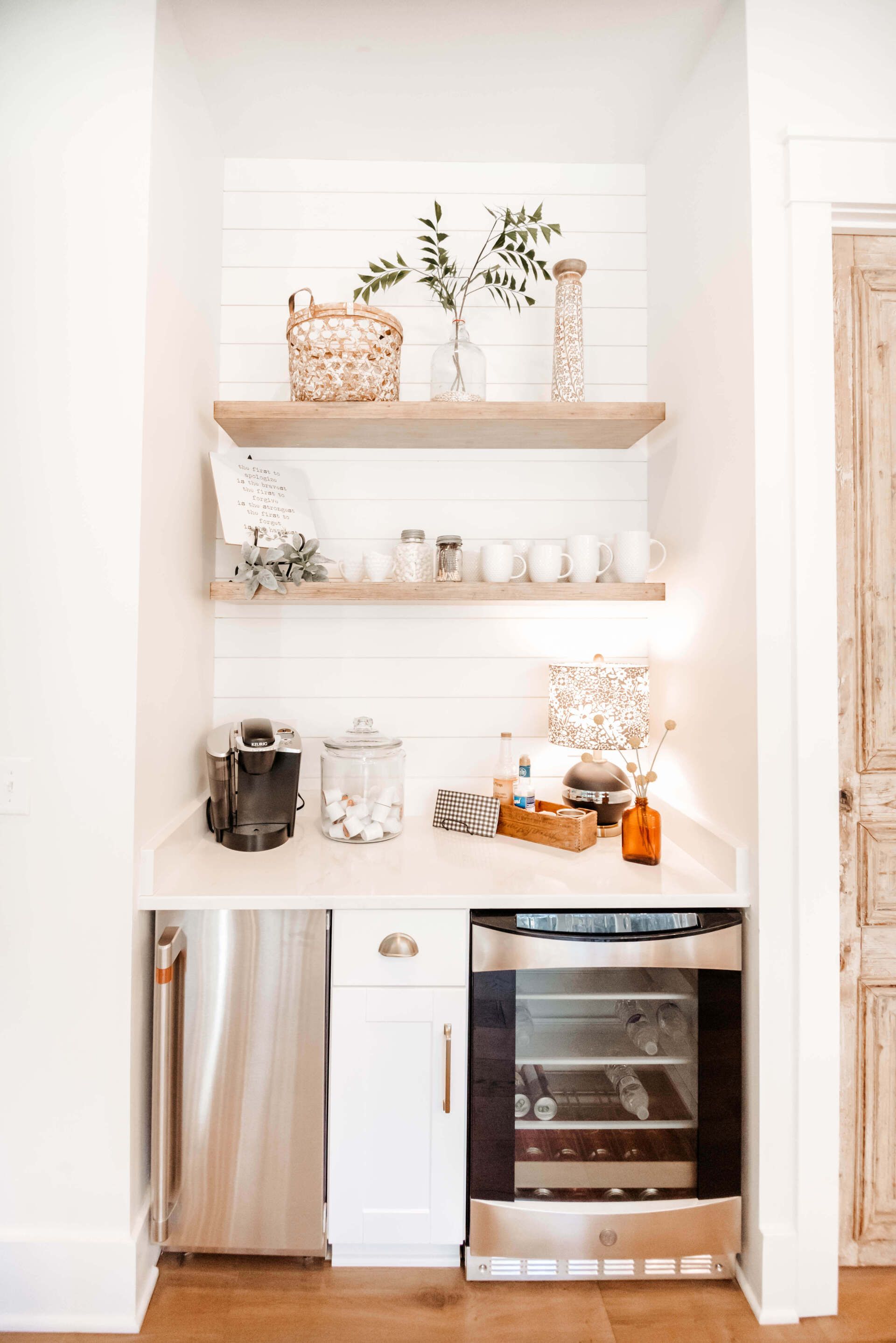 White kitchen nook with floating shelves, countertop appliances, and stainless steel mini fridge and oven