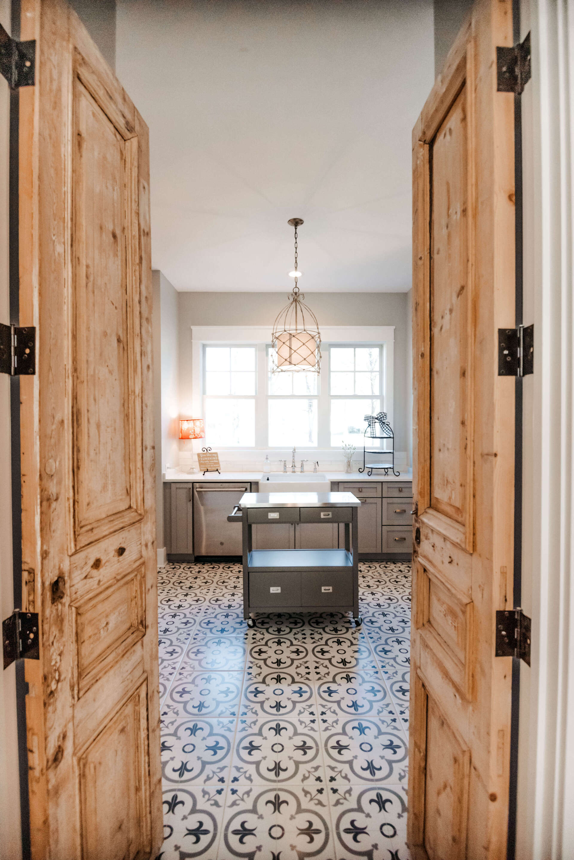 Open wooden doors framing a bright kitchen with patterned tile floor and large windows.
