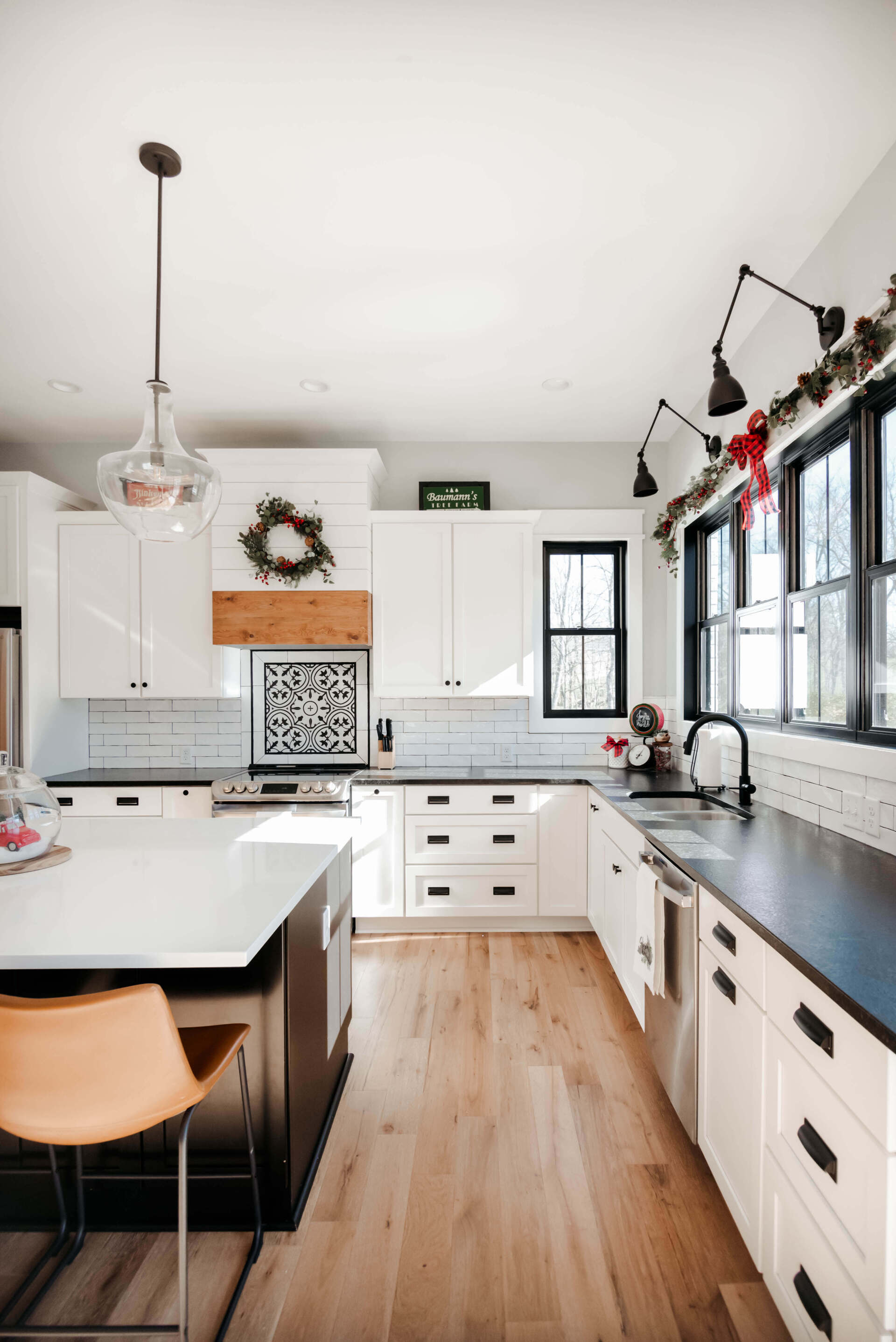 Bright modern kitchen with white cabinets, wood floors, black countertops, and pendant lights