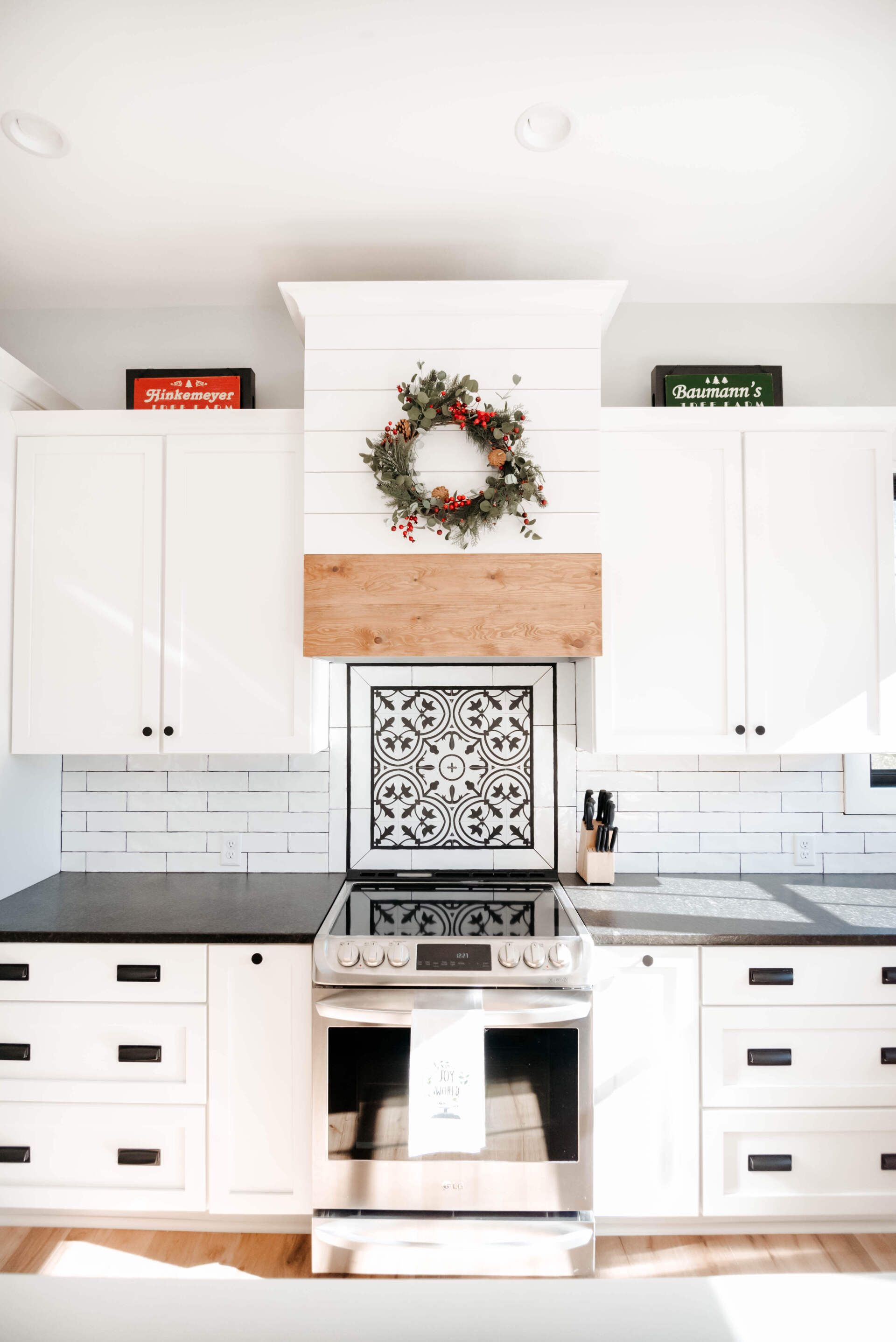 Bright white kitchen with stainless steel stove, white cabinets, and a wreath above a wooden range hood.