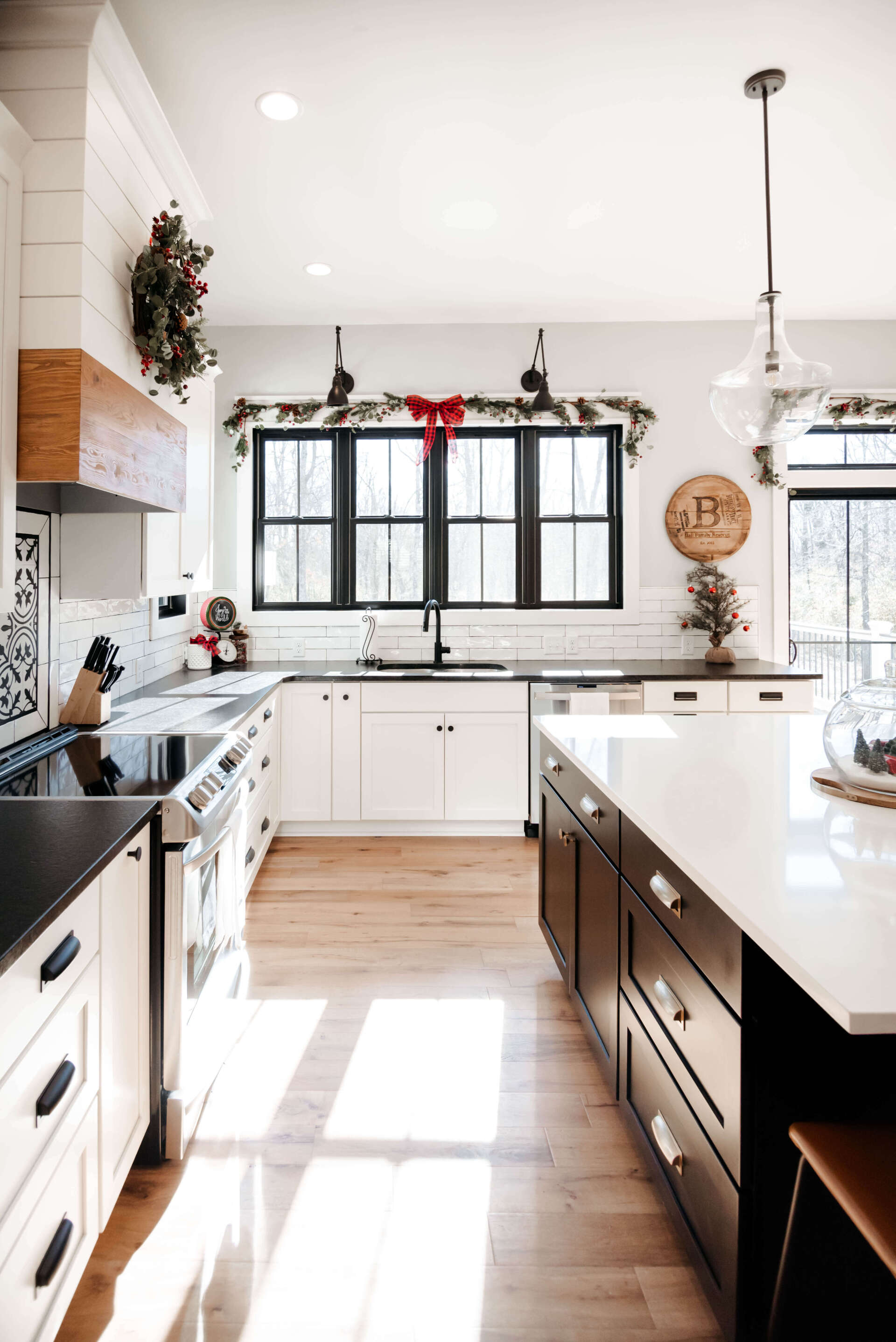 Bright, modern kitchen with white cabinets, dark island, and sunlit windows decorated for the holidays