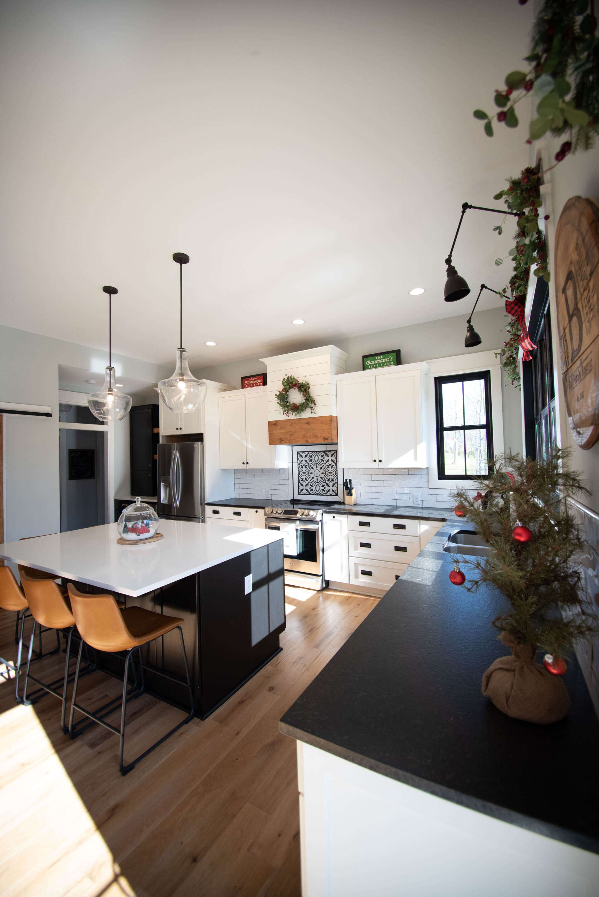 Bright modern kitchen with white cabinets, black countertops, island stools, and a small decorated tree.