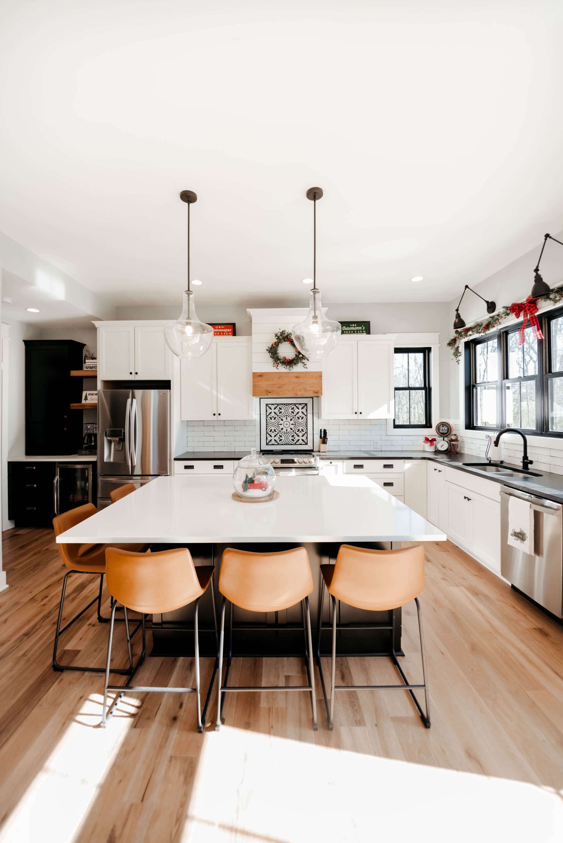 Bright modern kitchen with white cabinets, wood floors, and a large dining table with stools