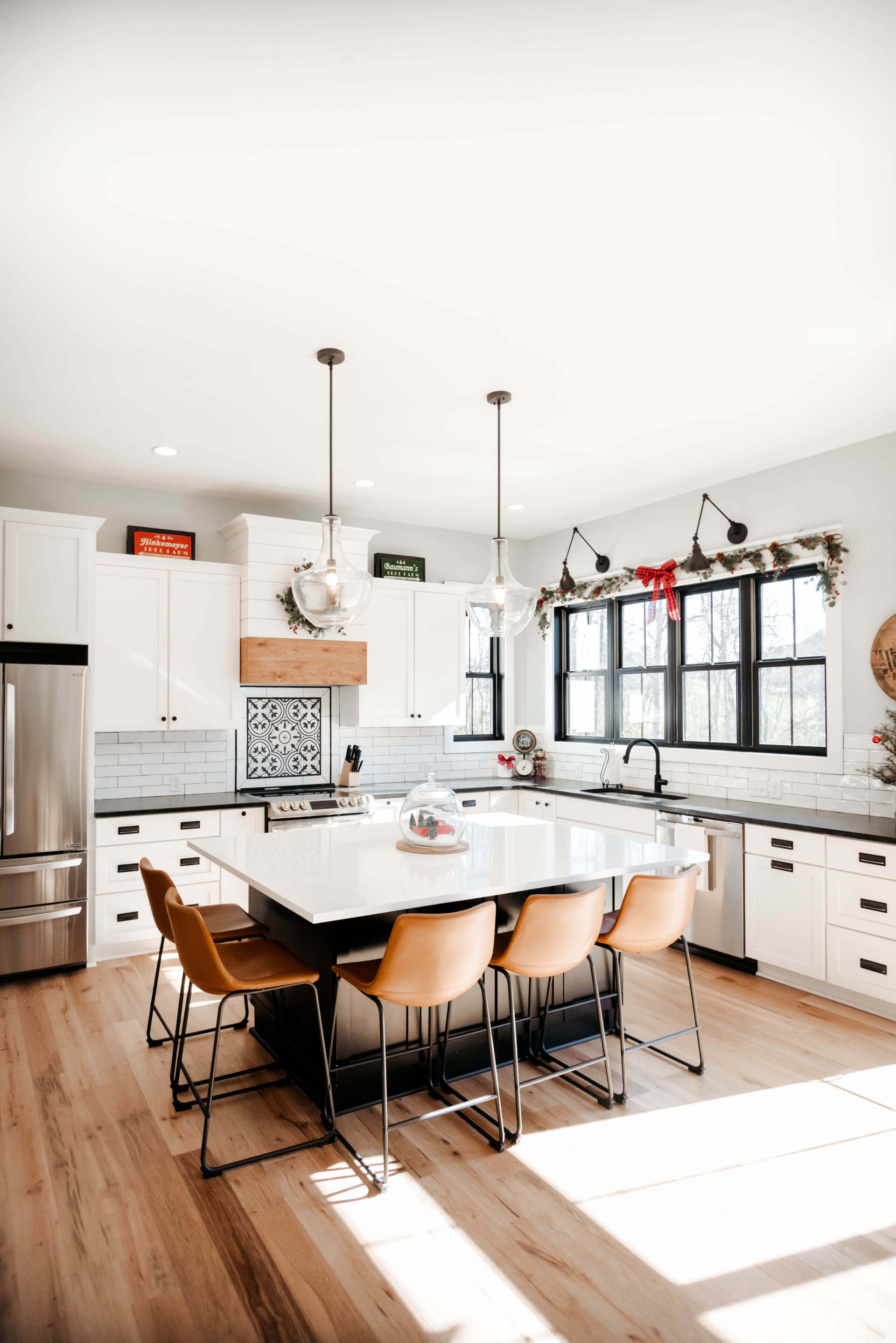 Bright modern kitchen with white cabinets, island seating, black-framed windows, and sunlit hardwood floors