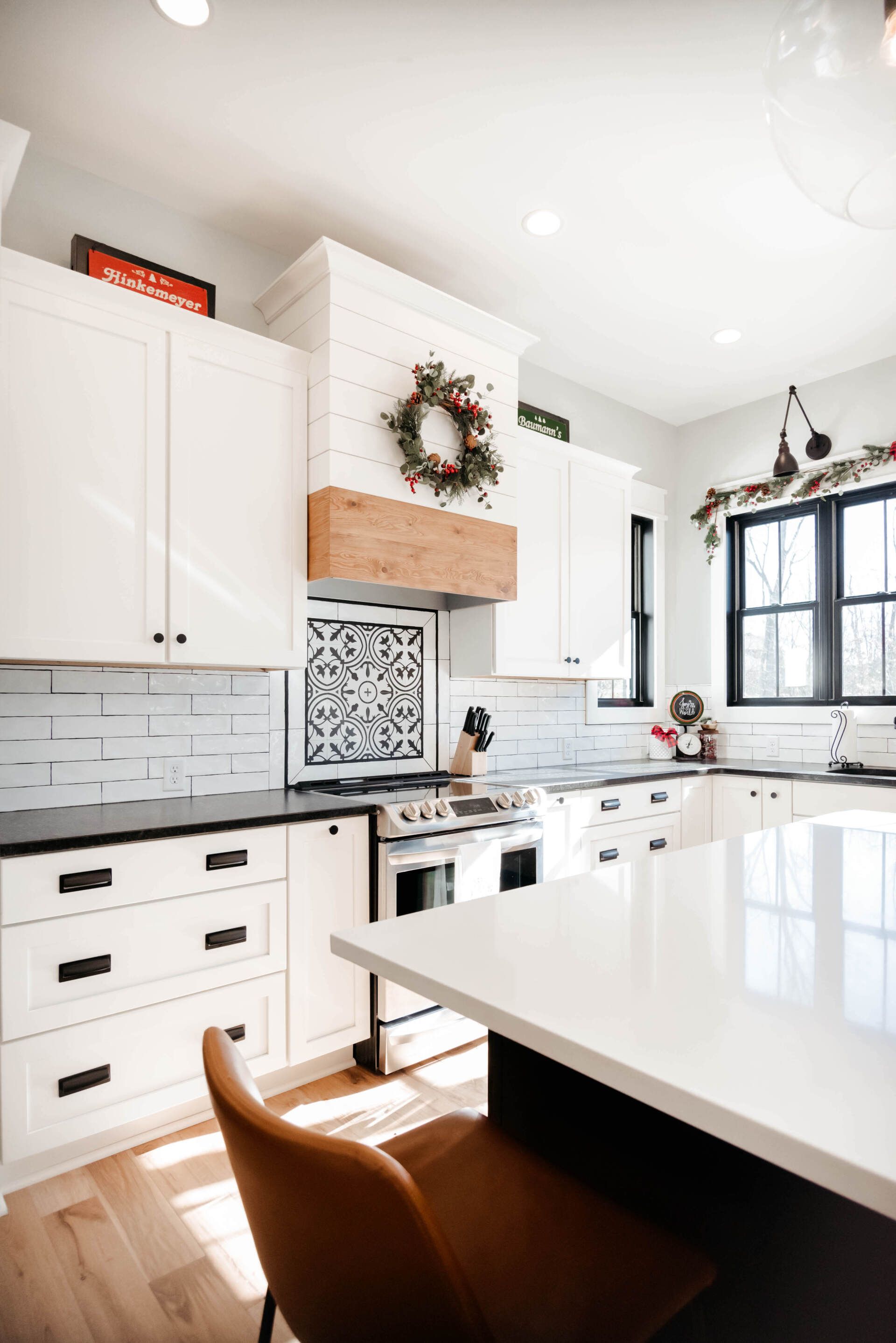 Bright white modern kitchen with marble island, black window trim, and a wreath above the stove