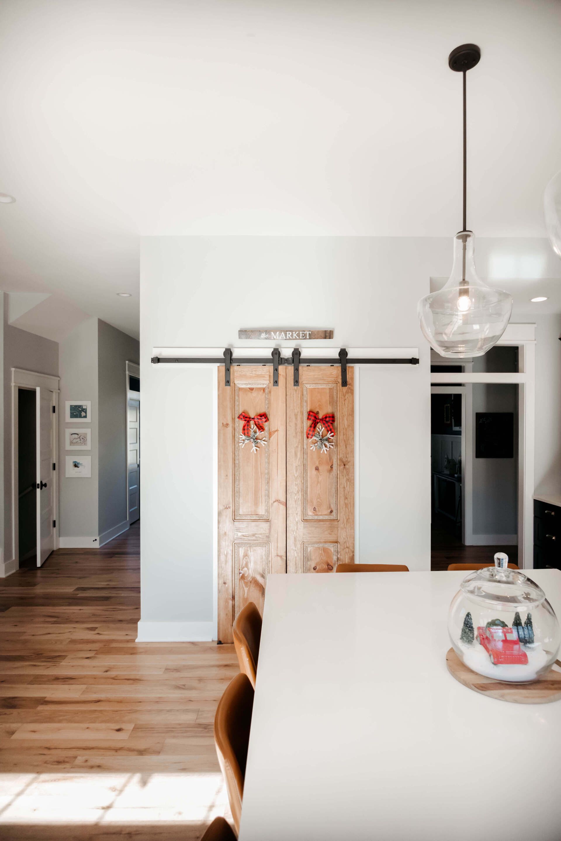 Bright kitchen with white island, wooden sliding barn doors, wood floor, and hanging glass pendant light.