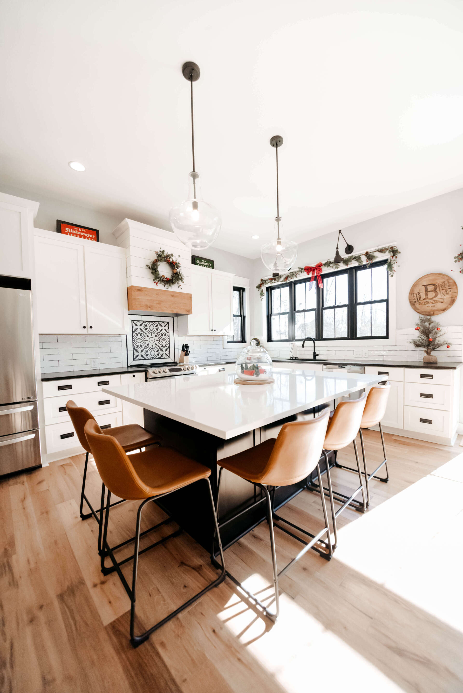 Bright modern kitchen with white cabinets, island, wooden chairs, and large black-framed window