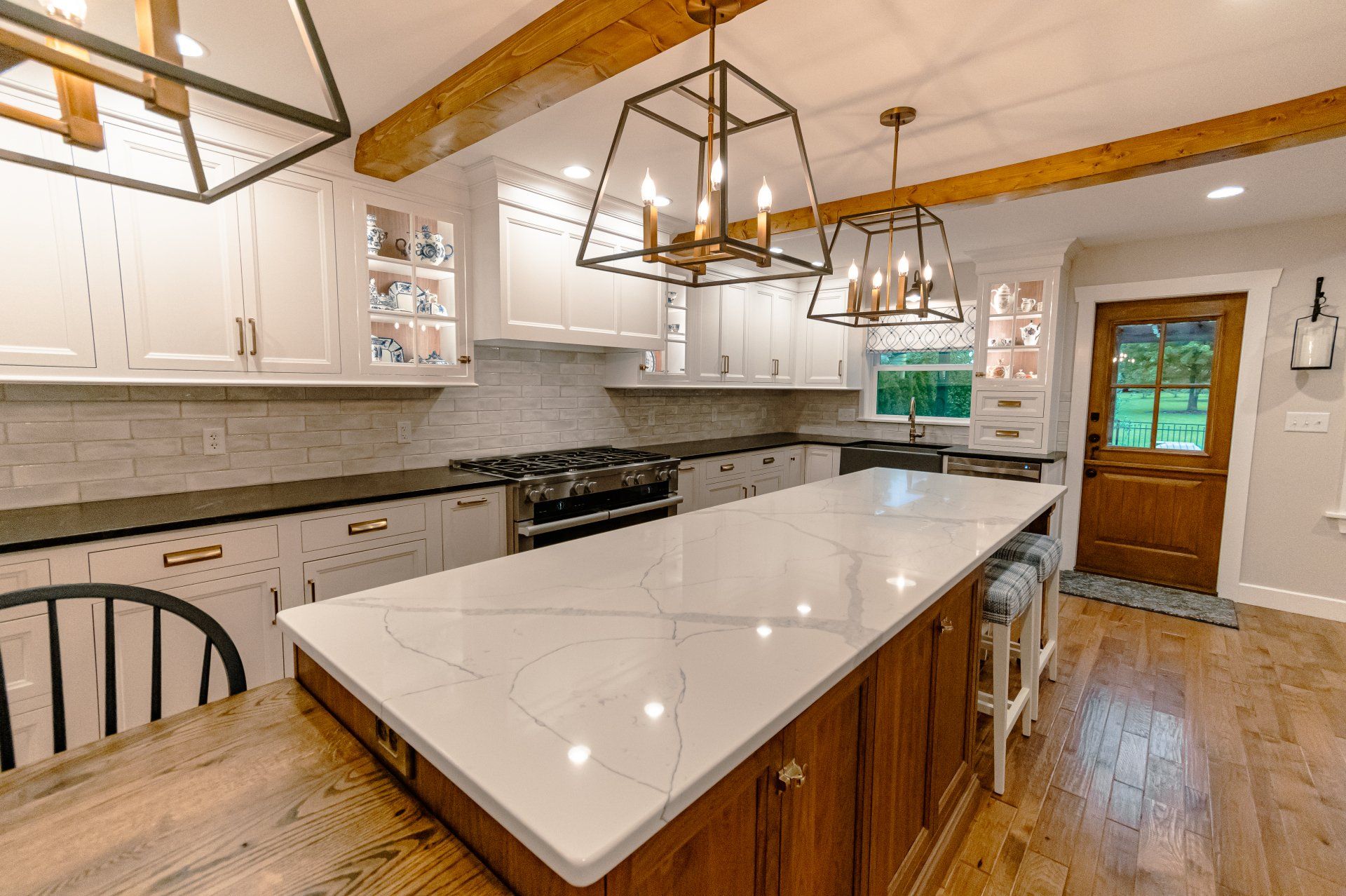Bright modern kitchen with large white island, brass pendant lights, white cabinets, and wood floor
