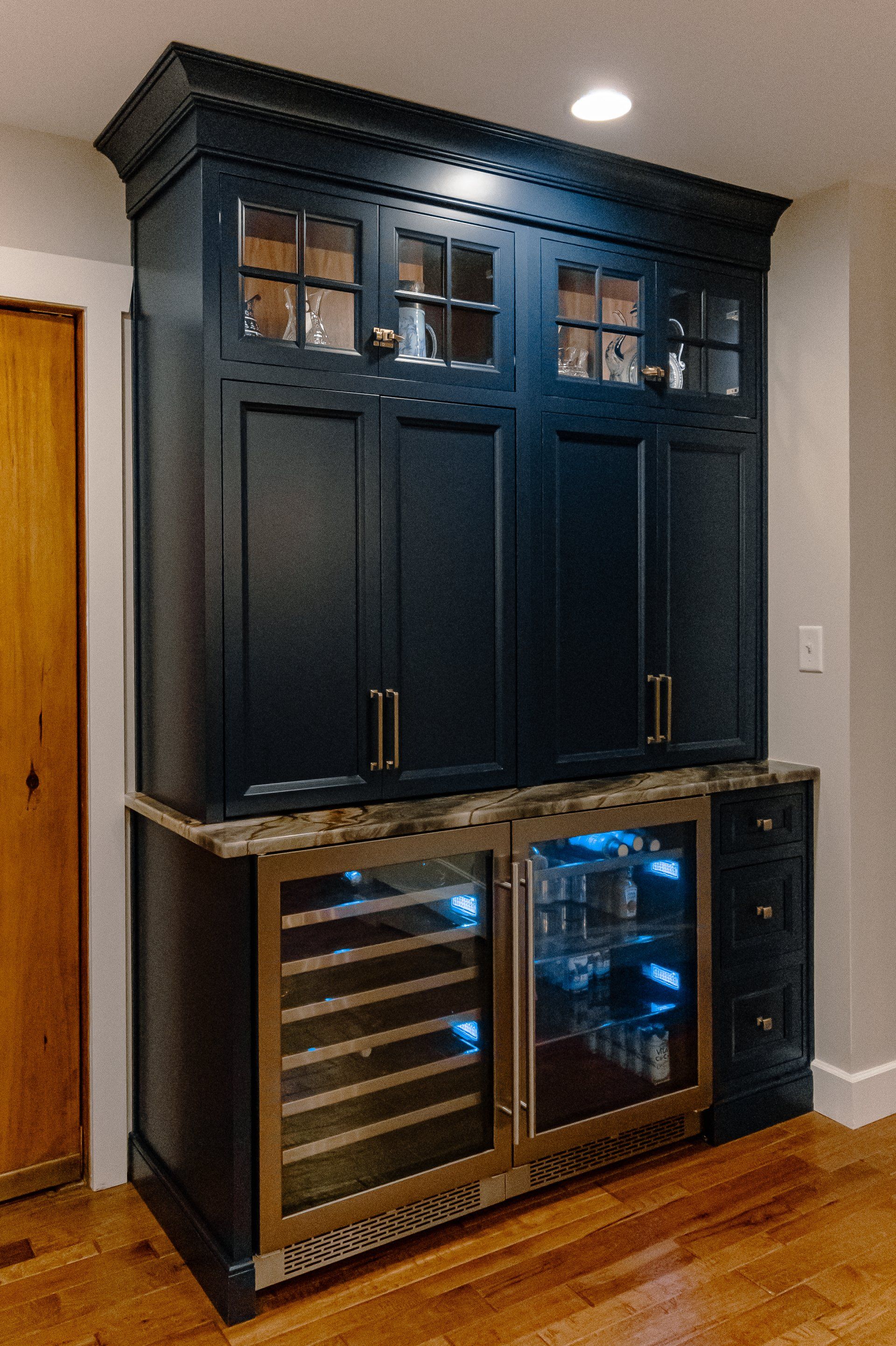 Dark blue built-in cabinet with granite counter and two glass-door wine fridges in a hardwood-floored room