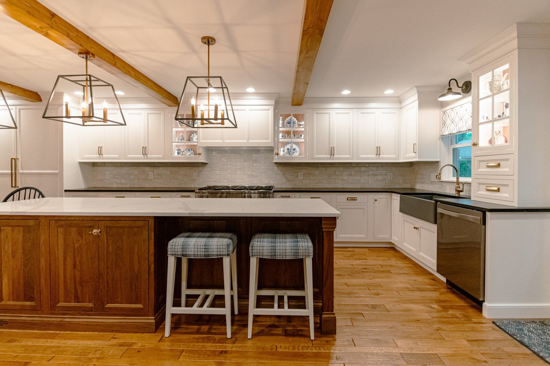 Modern white kitchen with wood island, two stools, pendant lights, and hardwood floors