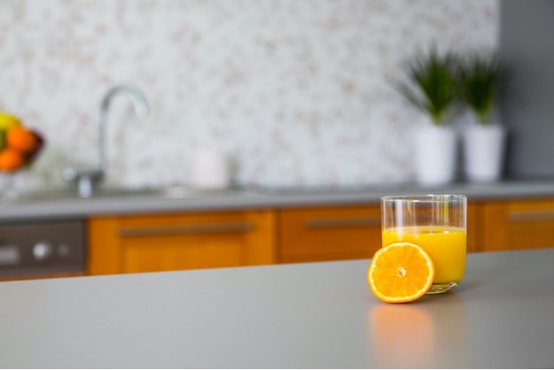 Glass of orange juice with a sliced orange on a kitchen counter