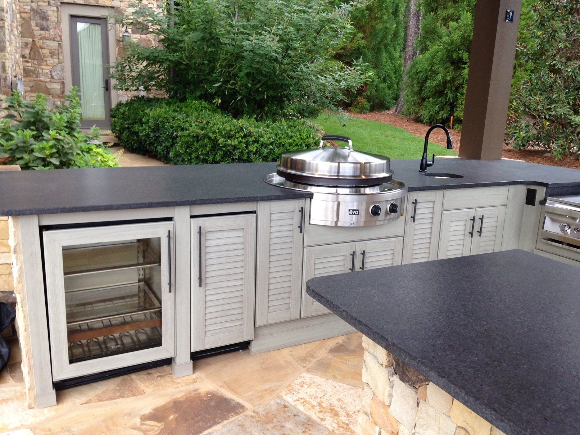 Outdoor kitchen with stainless grill, black countertop, and gray cabinets on a patio