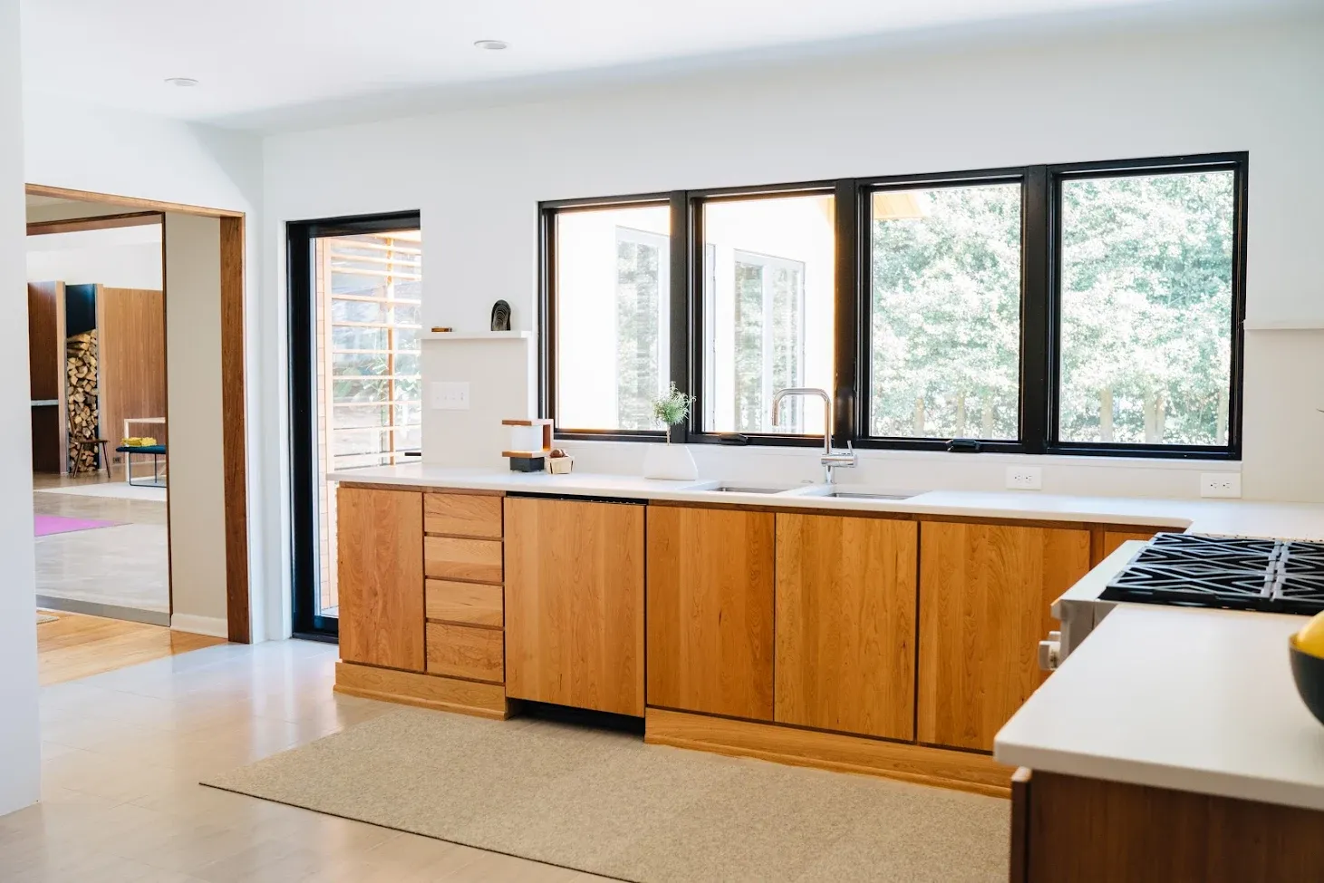 Modern kitchen with wood cabinets, white countertops, large windows, and a gas stove on the right.
