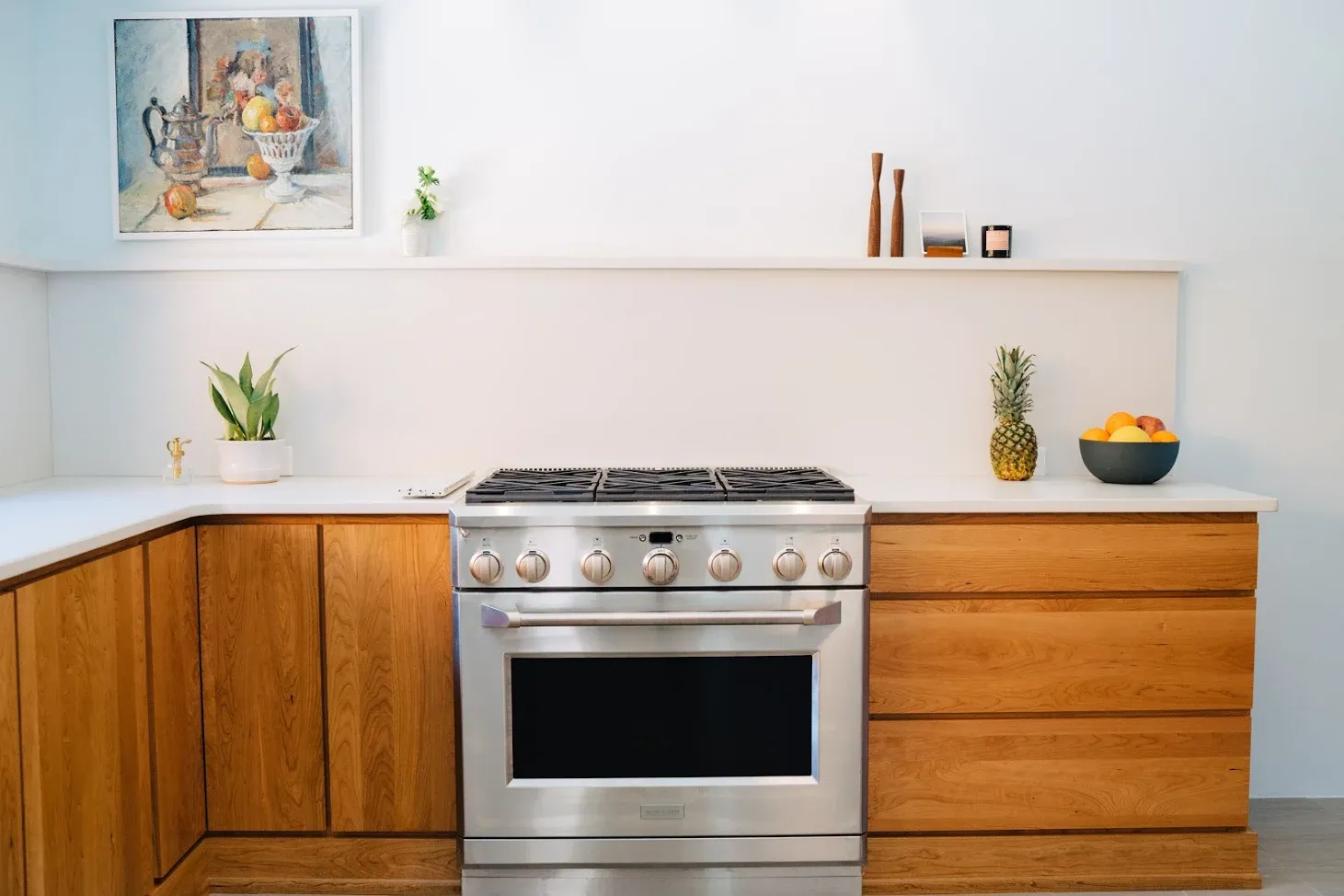 Modern kitchen with wooden cabinets, stainless steel stove, and small plants on white countertops