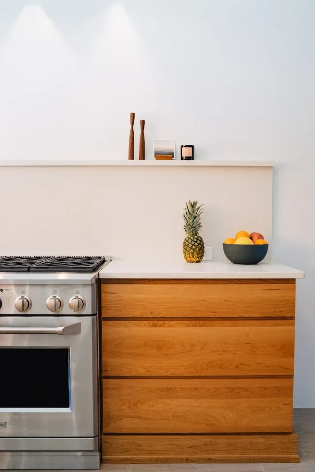 Modern kitchen with stainless stove, wooden cabinets, pineapple decor, and a bowl of fruit on the counter