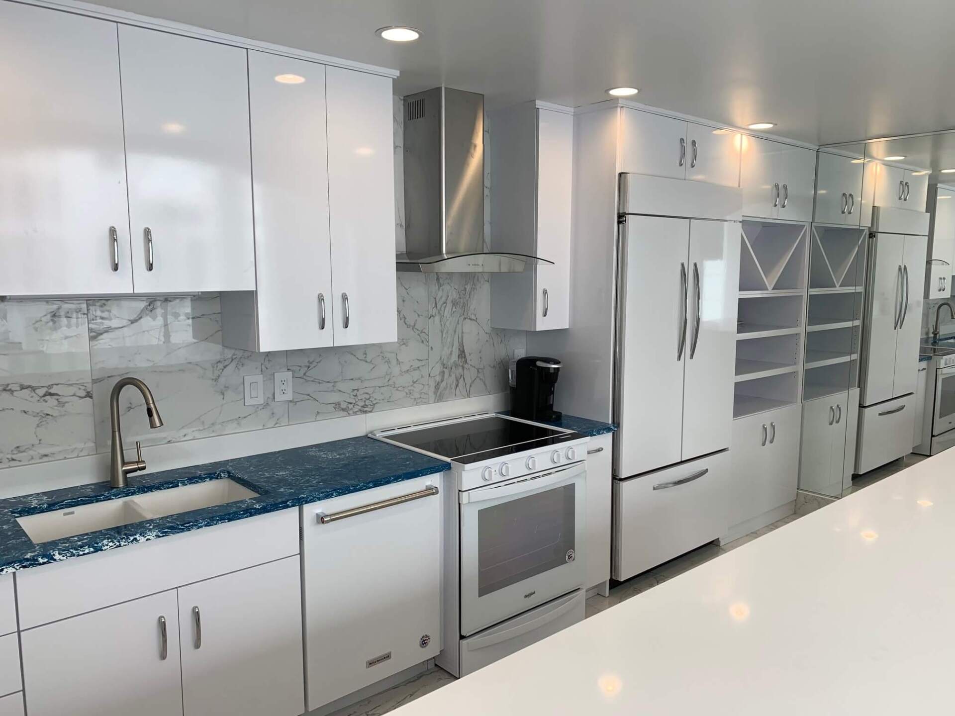 Modern white kitchen with marble backsplash, stainless appliances, and glossy cabinets