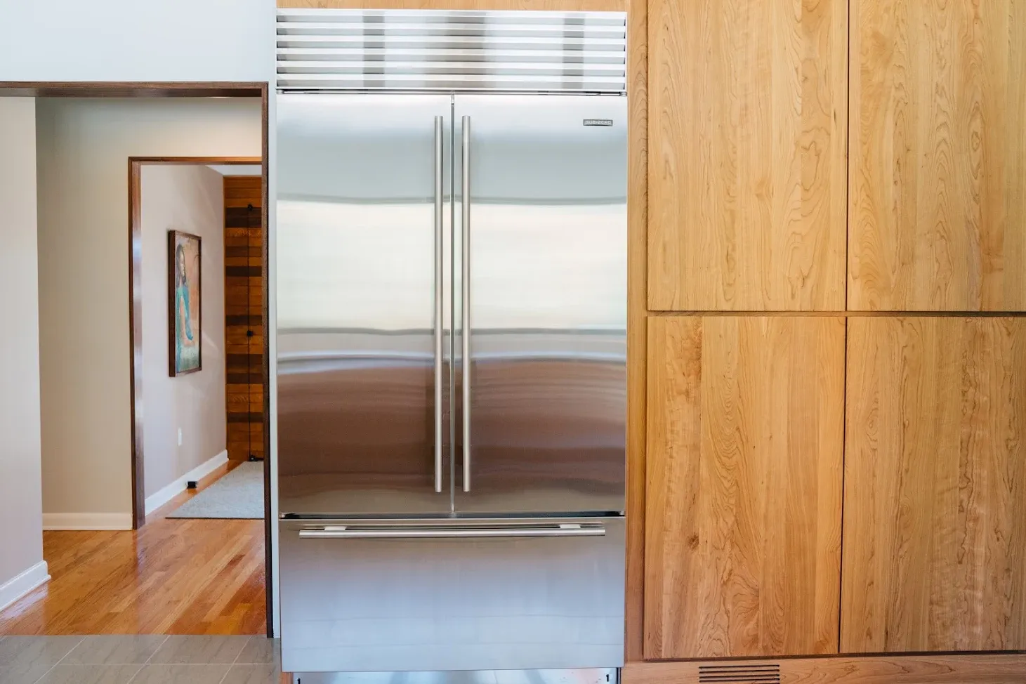 Stainless steel refrigerator beside wood kitchen cabinets and a doorway to a hallway