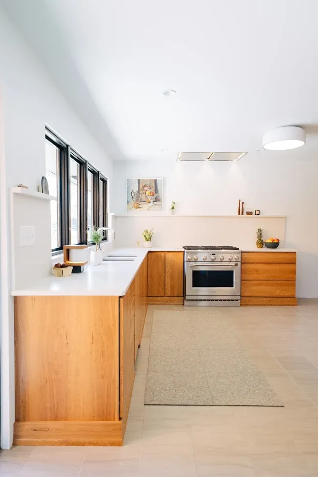 Bright modern kitchen with white countertops, wood cabinets, and a large window wall