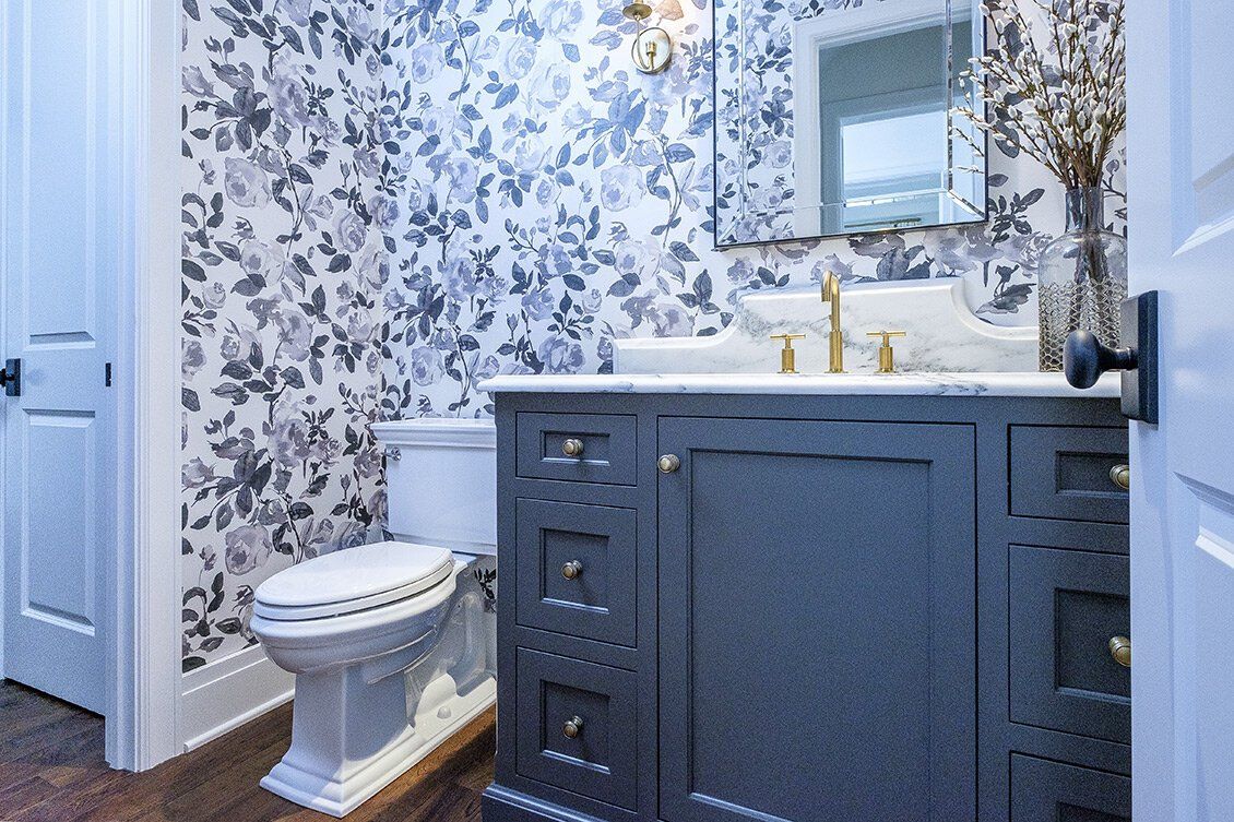 Modern bathroom with blue vanity, floral wallpaper, white toilet, and gold faucet under a mirror