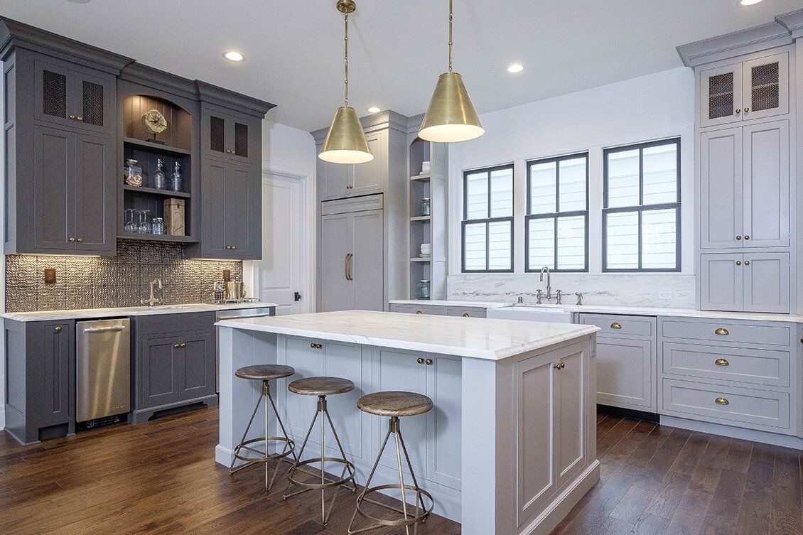 Modern white kitchen with a large island, bar stools, gray cabinets, and pendant lights