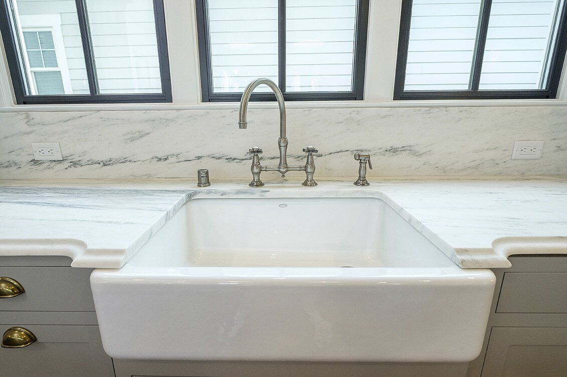 White farmhouse sink beneath windows with a chrome faucet in a bright kitchen
