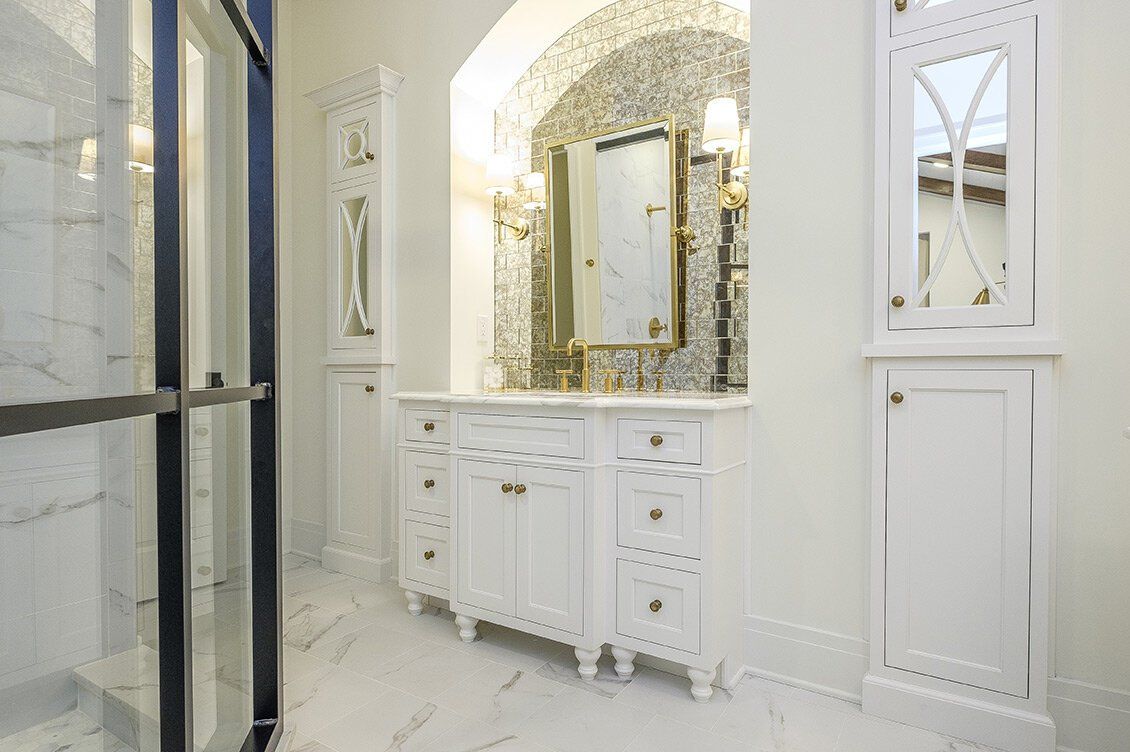 White marble bathroom vanity with gold mirror and glass shower door