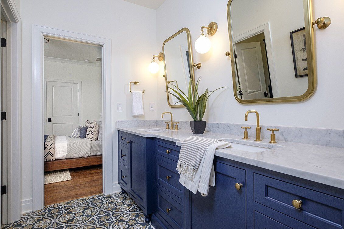 Blue bathroom vanity with gold fixtures, patterned floor tile, and a doorway to a bedroom.